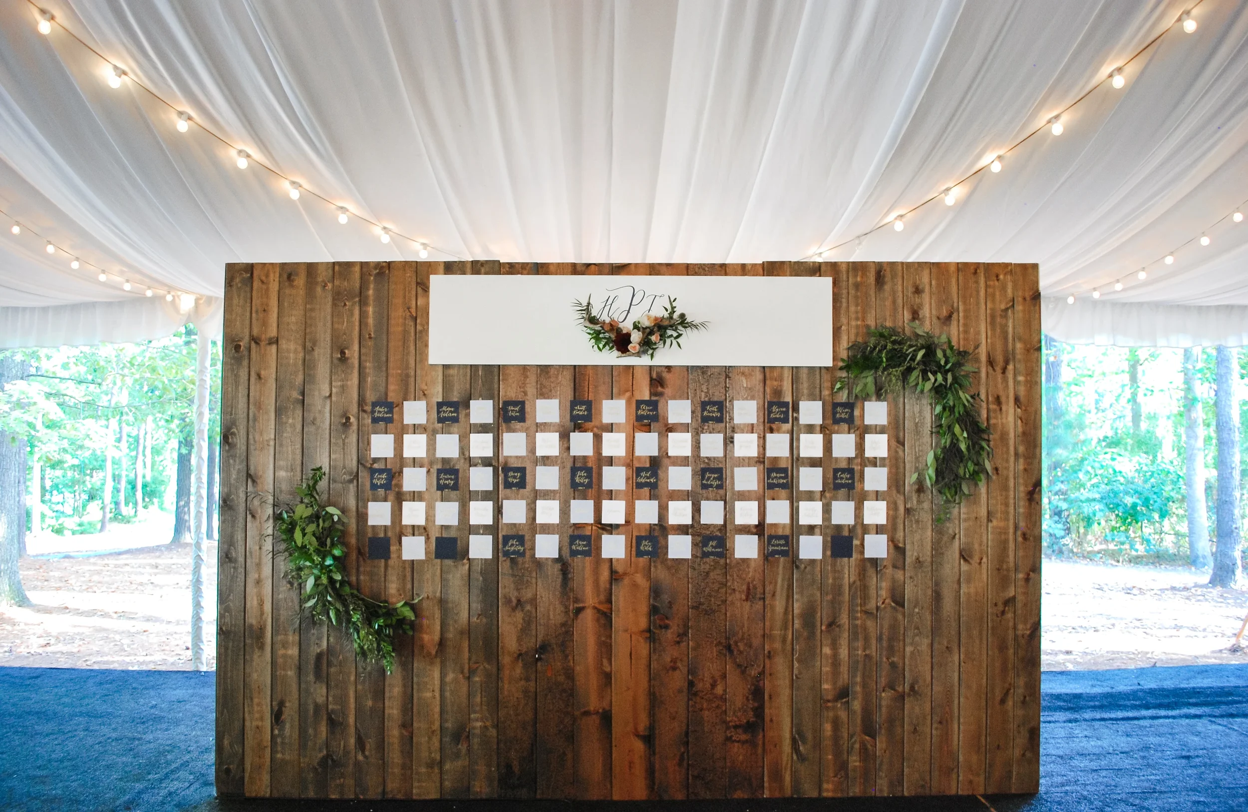 Rustic lodge-inspired wedding escort card wall with a custom monogram antler crest and gold foil calligraphed guest cards.