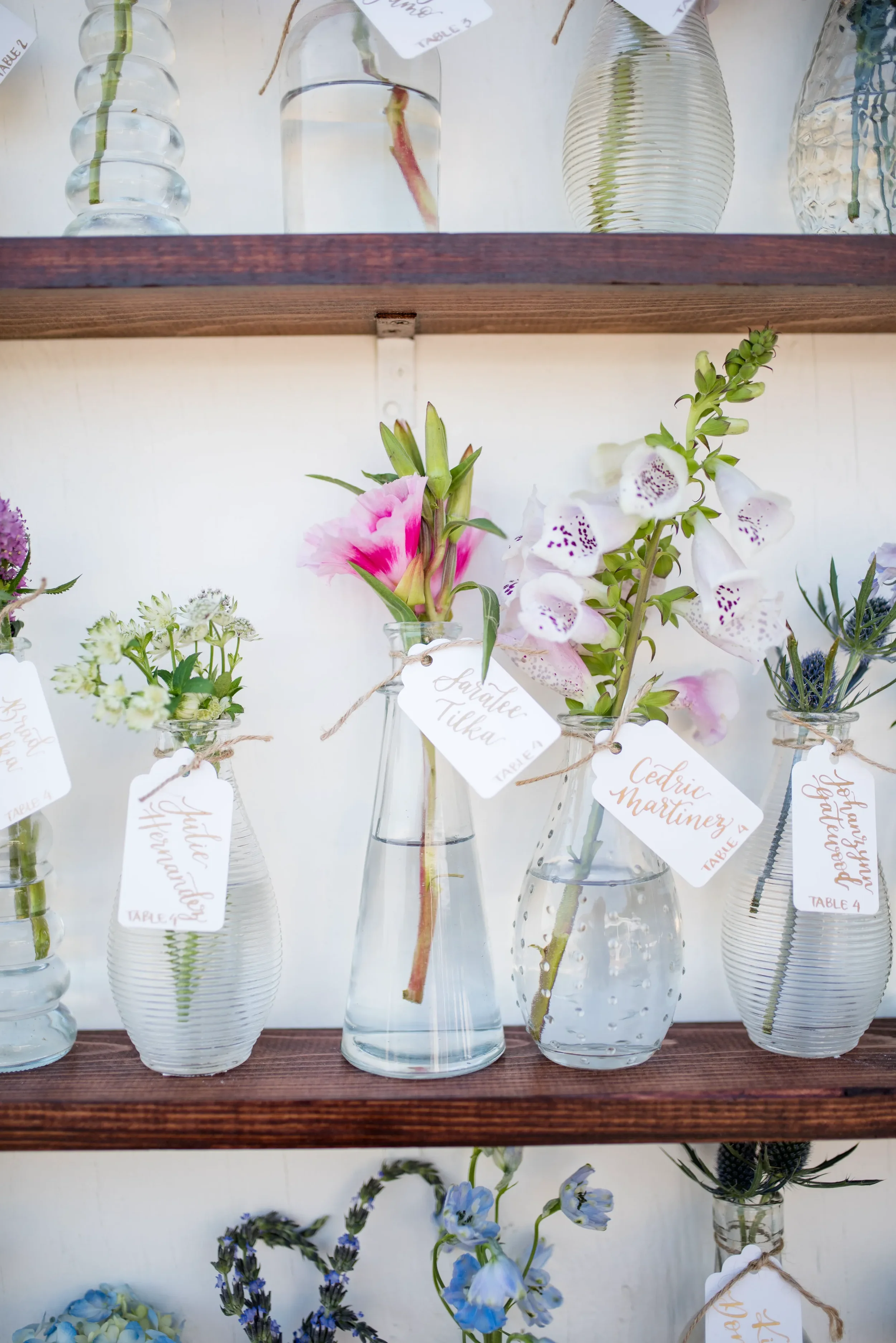 Elevate your reception decor using delicate, custom calligraphy tags styled on fresh floral bud vases. Perfect for an outdoor or garden celebration, this unique seating assignment idea seamlessly blends elegant stationery with organic design.