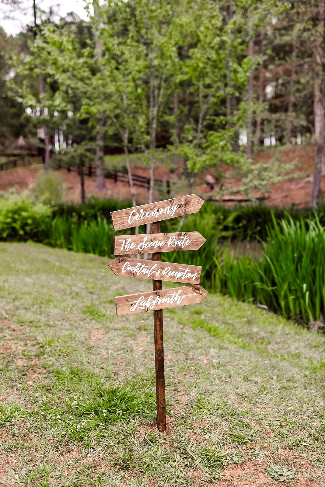 Outdoor wooden arrow signpost pointing guests toward the ceremony, reception, and lawn games.