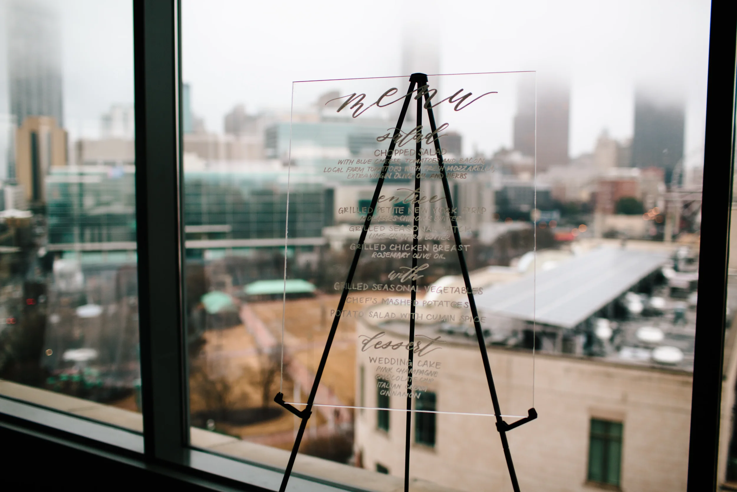 Clear acrylic wedding menu sign with white script calligraphy at an Atlanta city reception.