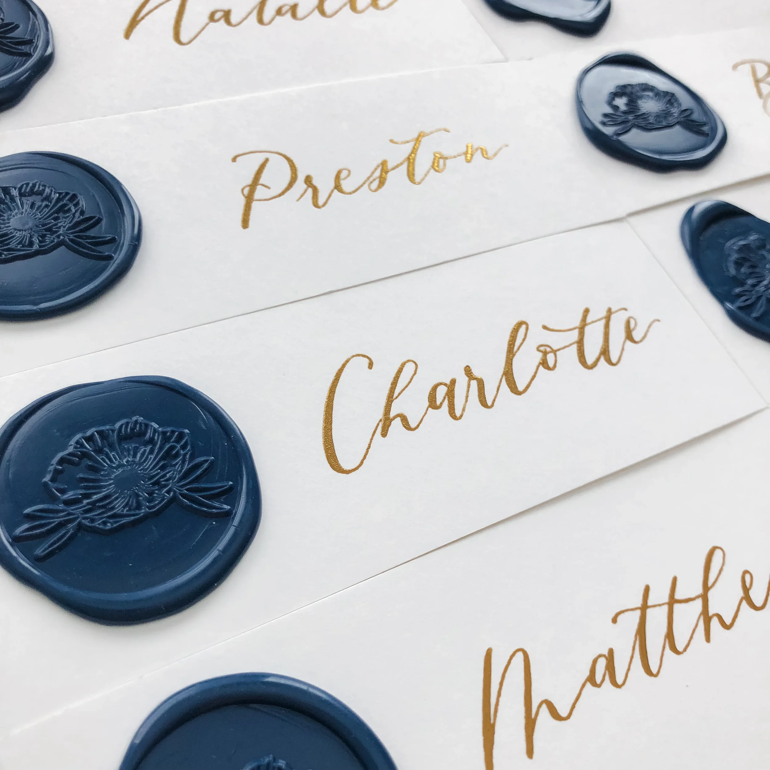 White paper escort ribbon strips with luxury gold calligraphy script and custom navy blue floral wax seals.