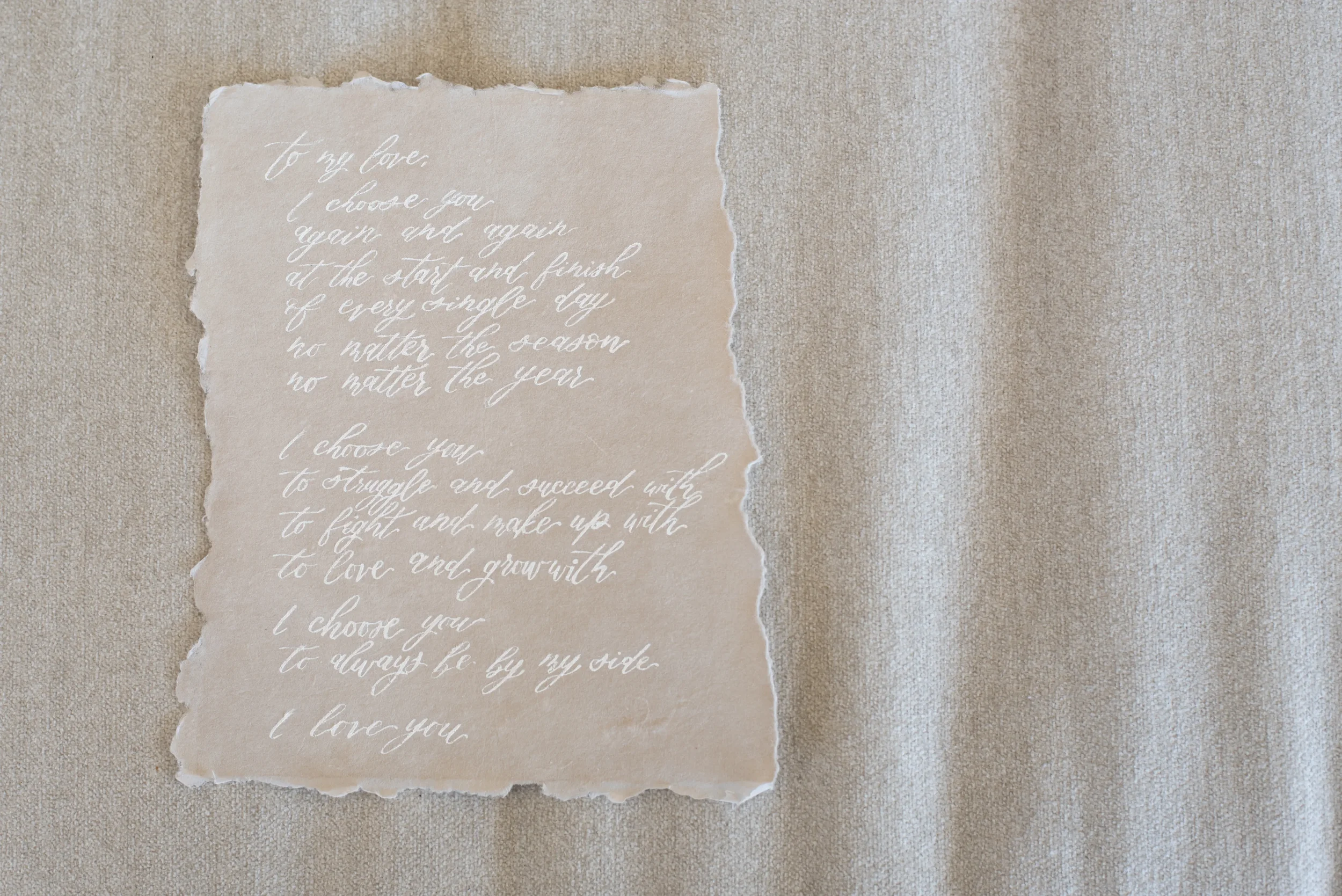 Custom white ink wedding vows calligraphy letter displayed flat on beige neutral linen.