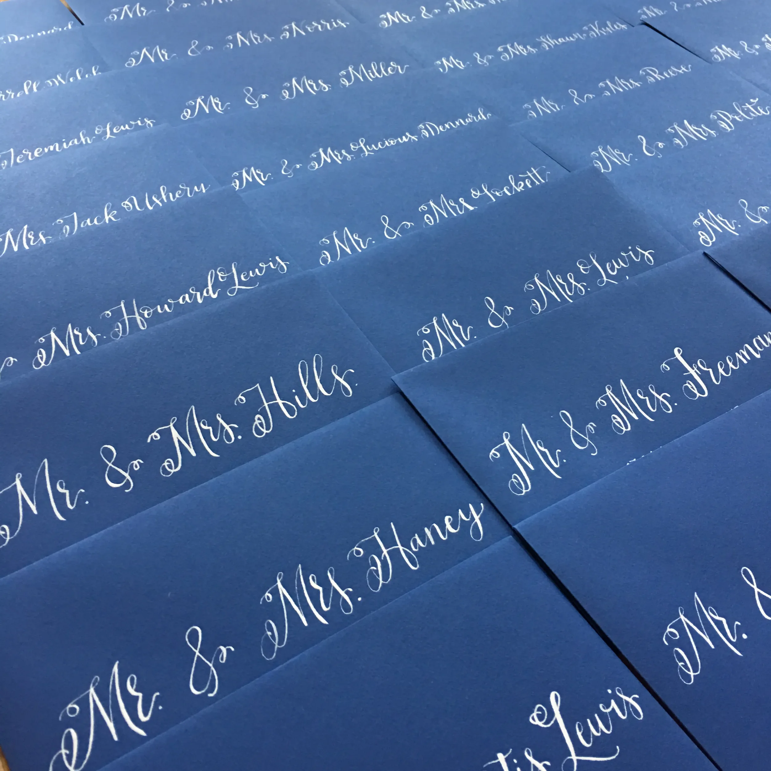 The striking contrast of crisp white ink calligraphy script on the dark blue cardstock provides a timeless exterior for any wedding or occasion.