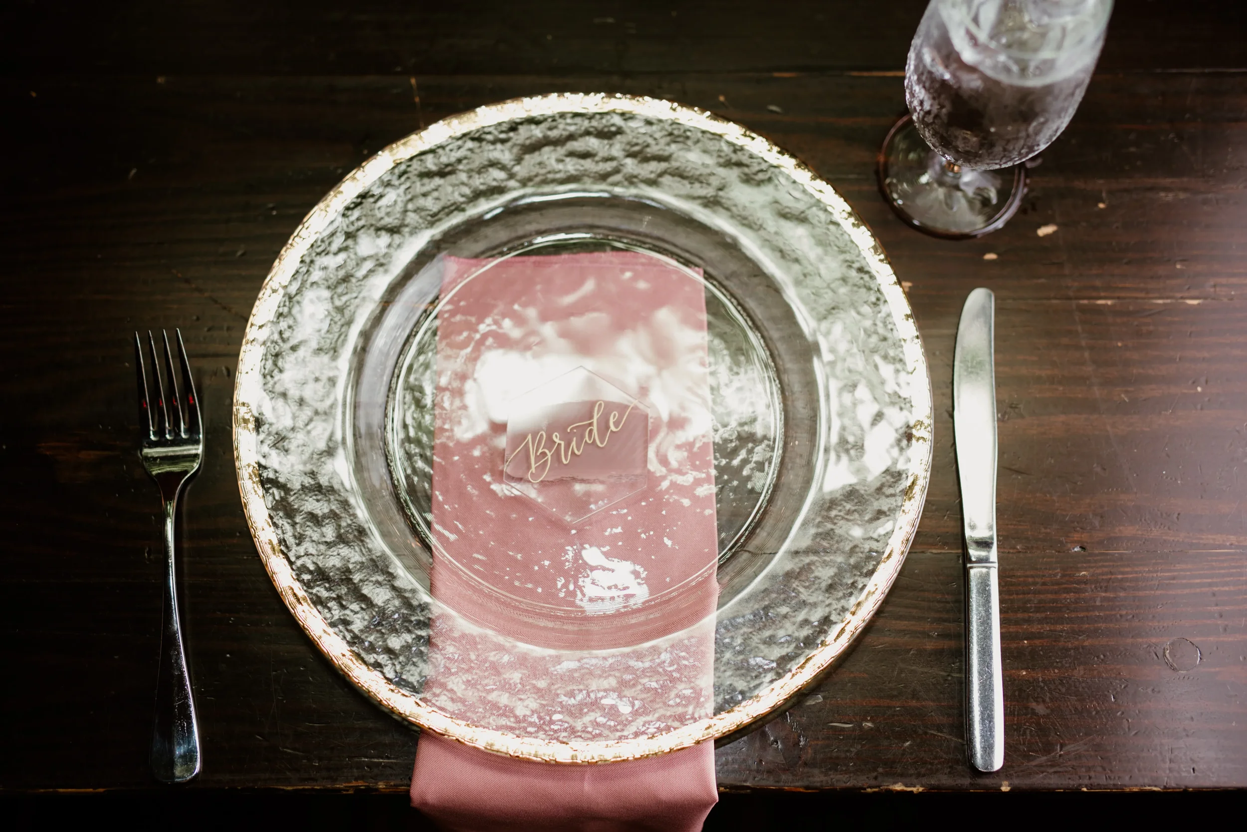 Painted-back clear acrylic hexagon place card with gold script calligraphy on a metallic-rimmed plate.