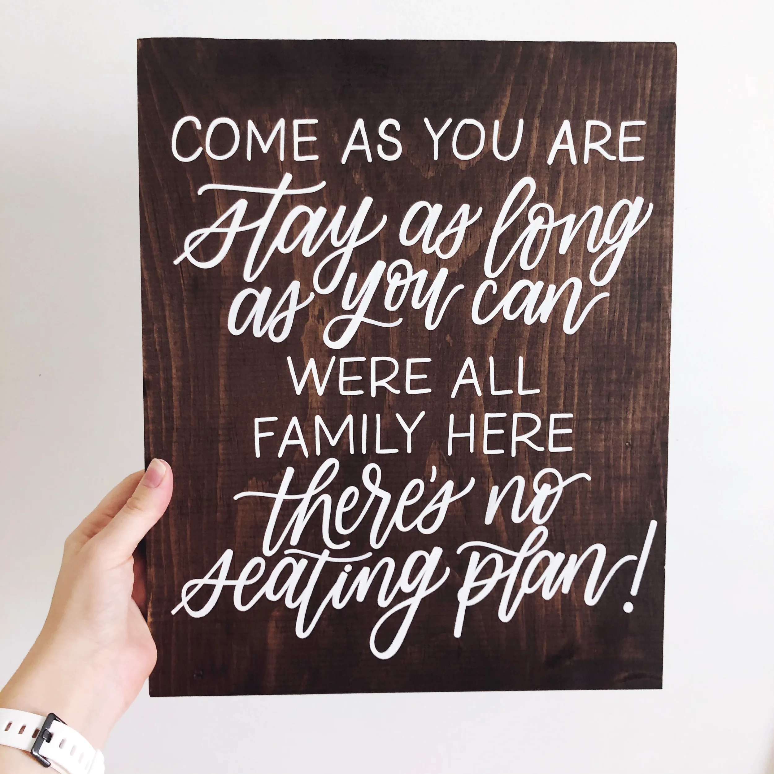 Hand-held stained wooden sign offering a friendly message for open seating at a wedding reception.