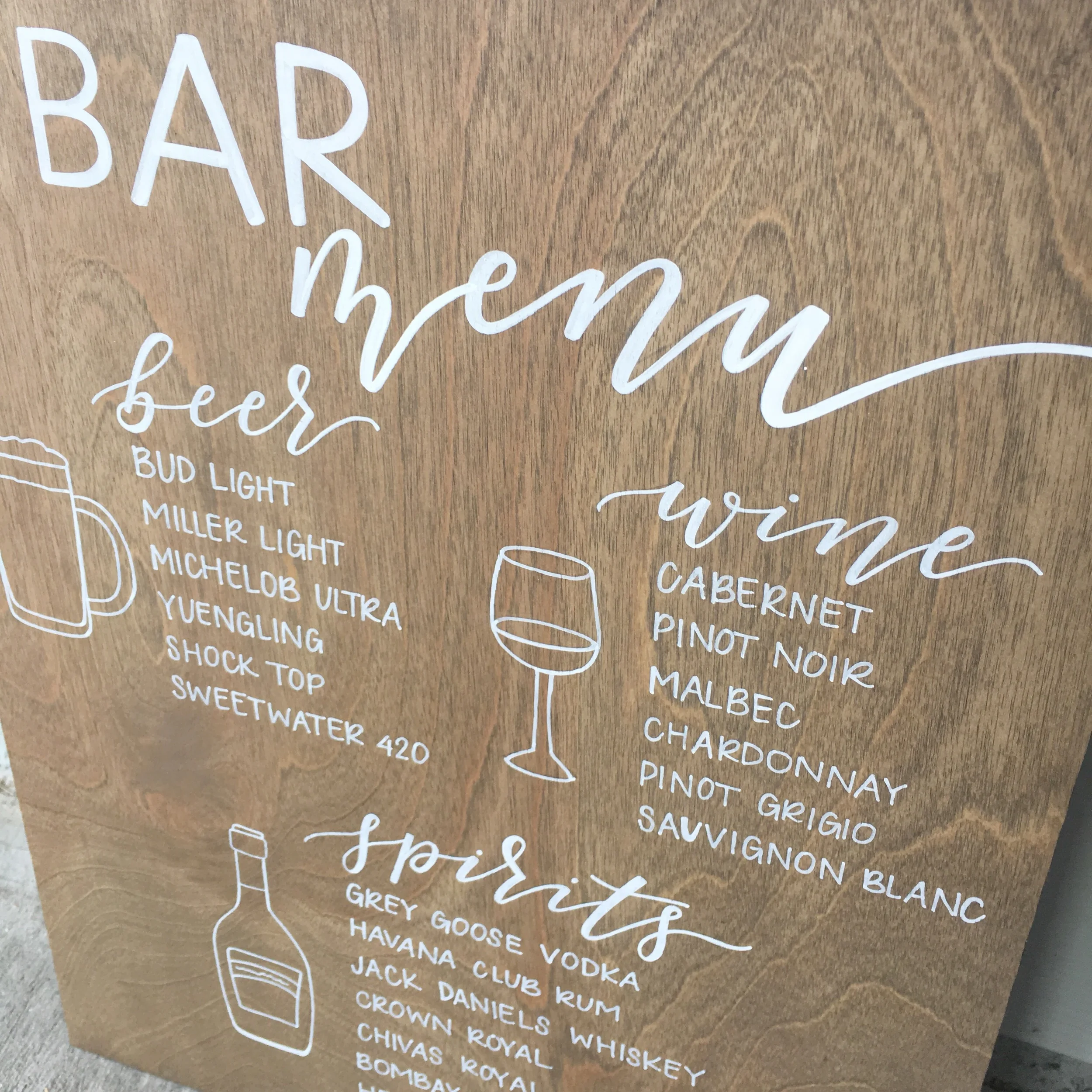 Hand-lettered wooden reception drink menu board with illustrated beer mug and wine glass details.