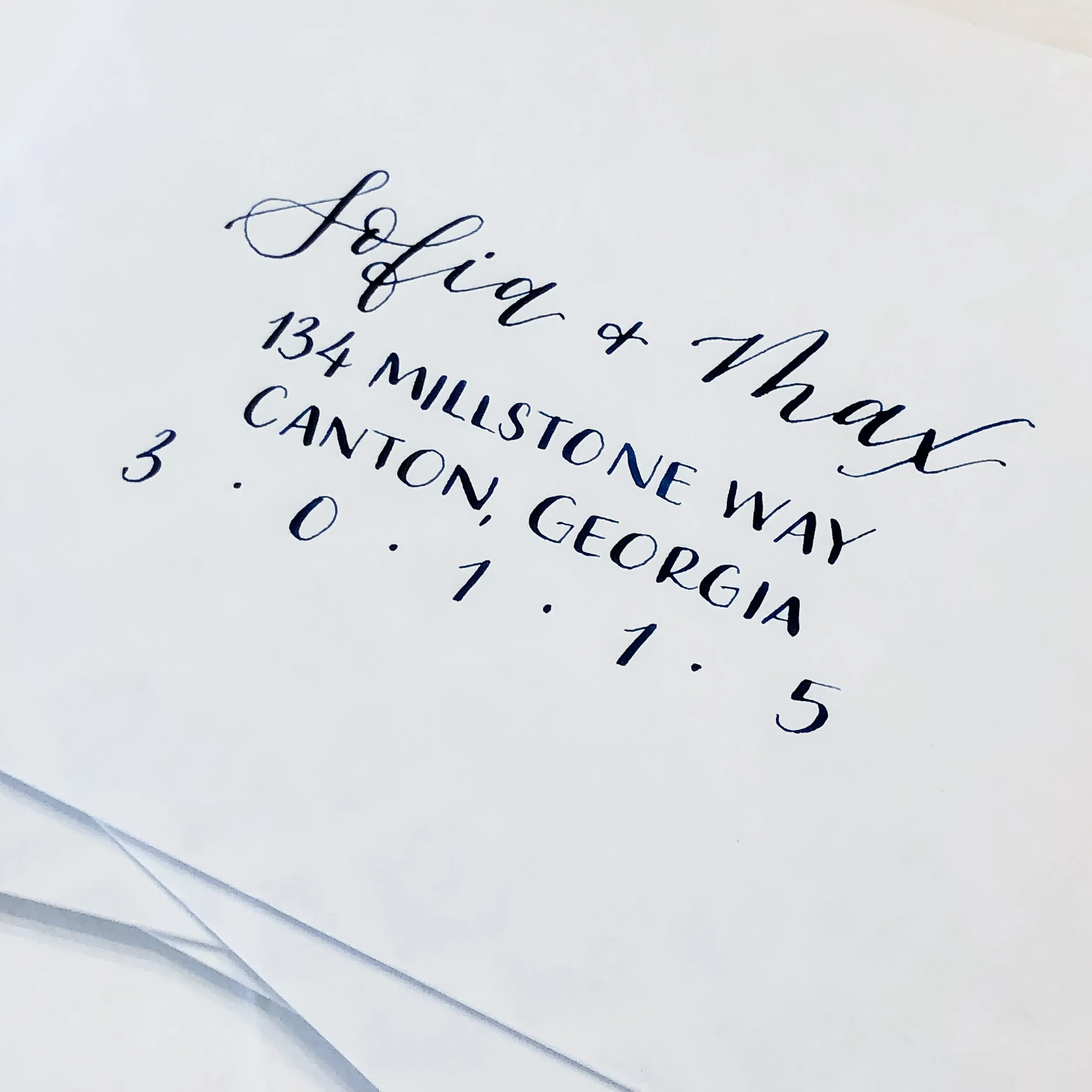 Minimalist white wedding invitation envelope featuring modern script calligraphy and spaced block-font addressing.