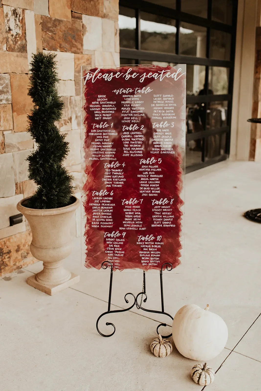Large burgundy painted-back acrylic with white lettering wedding seating chart on a scroll easel.