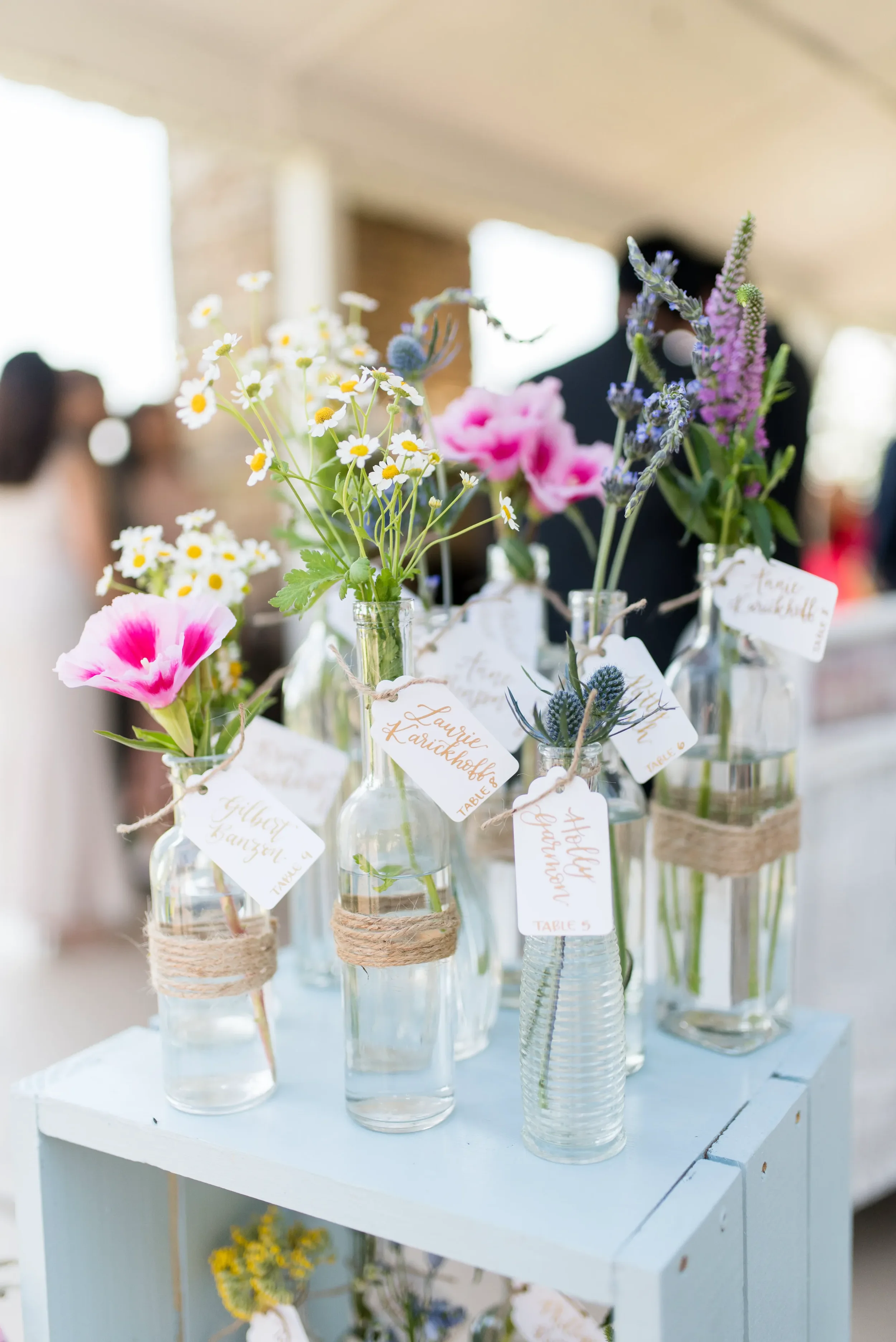 Bring a whimsical, fine-art feel to your Georgia countryside reception with an interactive floral seating chart. Our hand-lettered escort tags add a personalized, luxurious touch to rustic wooden shelving and mismatched clear glass vases.
