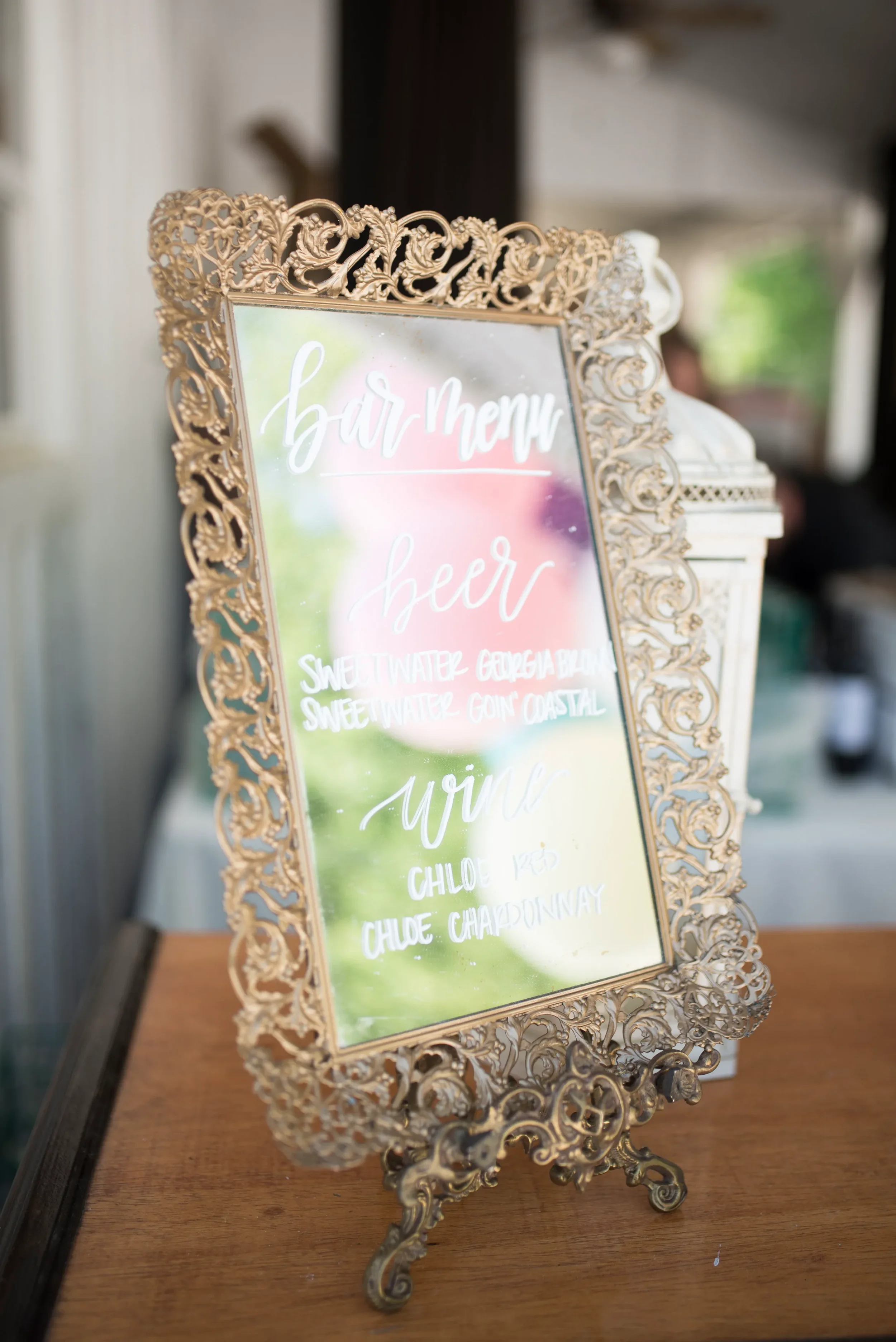Custom hand-lettered signature mocktails menu on a vintage ornate gold mirror at a Georgia wedding reception.