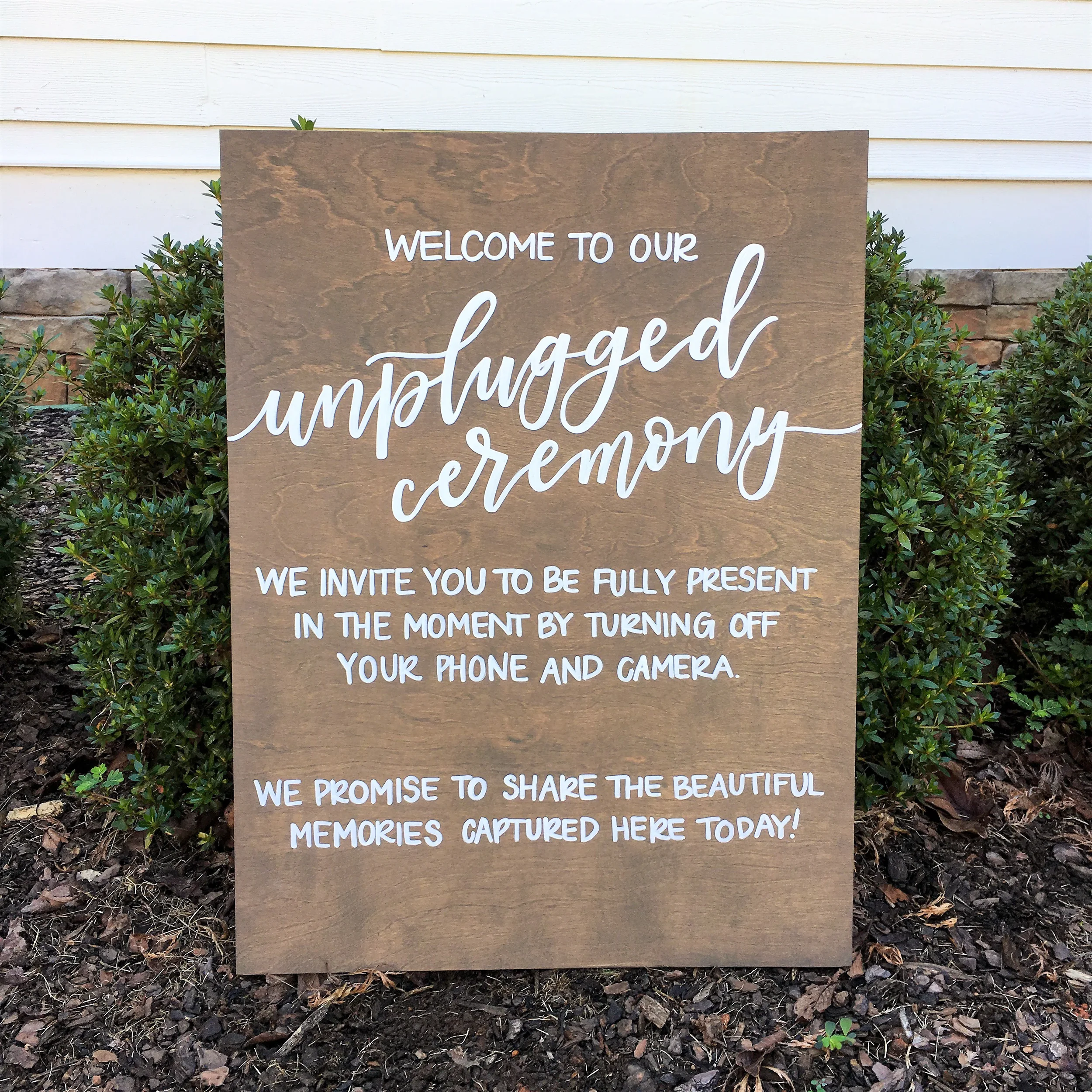 Vertical stained wood sign with white script and block lettering reading "Welcome to our unplugged ceremony".