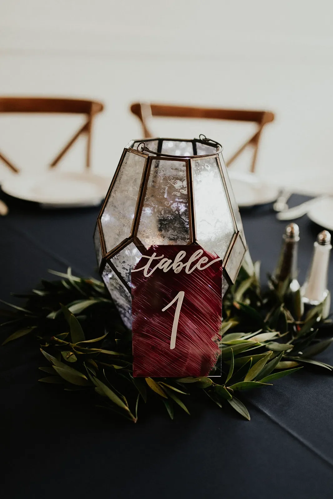 Burgundy acrylic table number 1 leaning against a geometric mercury glass lantern.