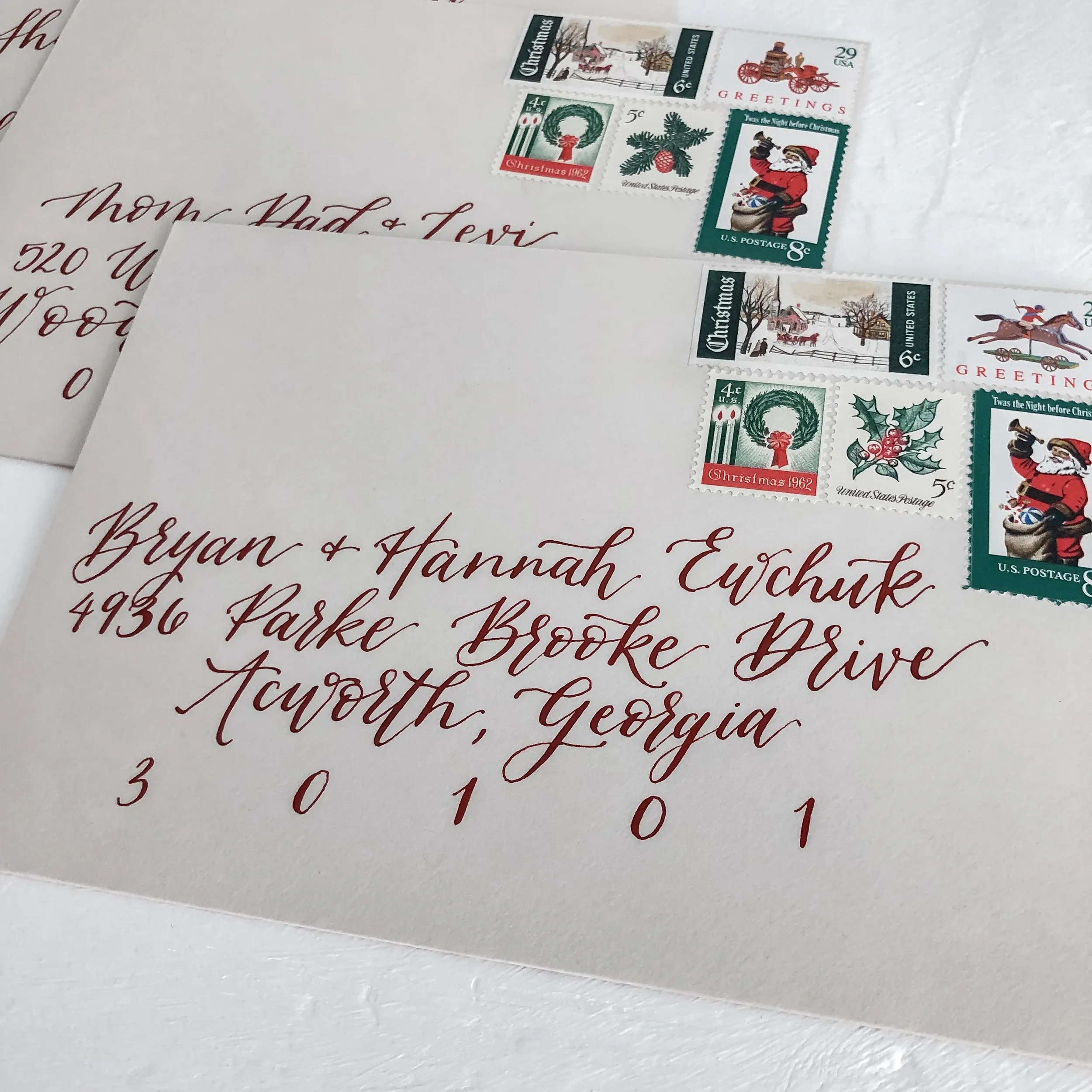 Gray kraft paper envelopes addressed in a deep burgundy calligraphy font with vintage Christmas stamps for Christmas cards.