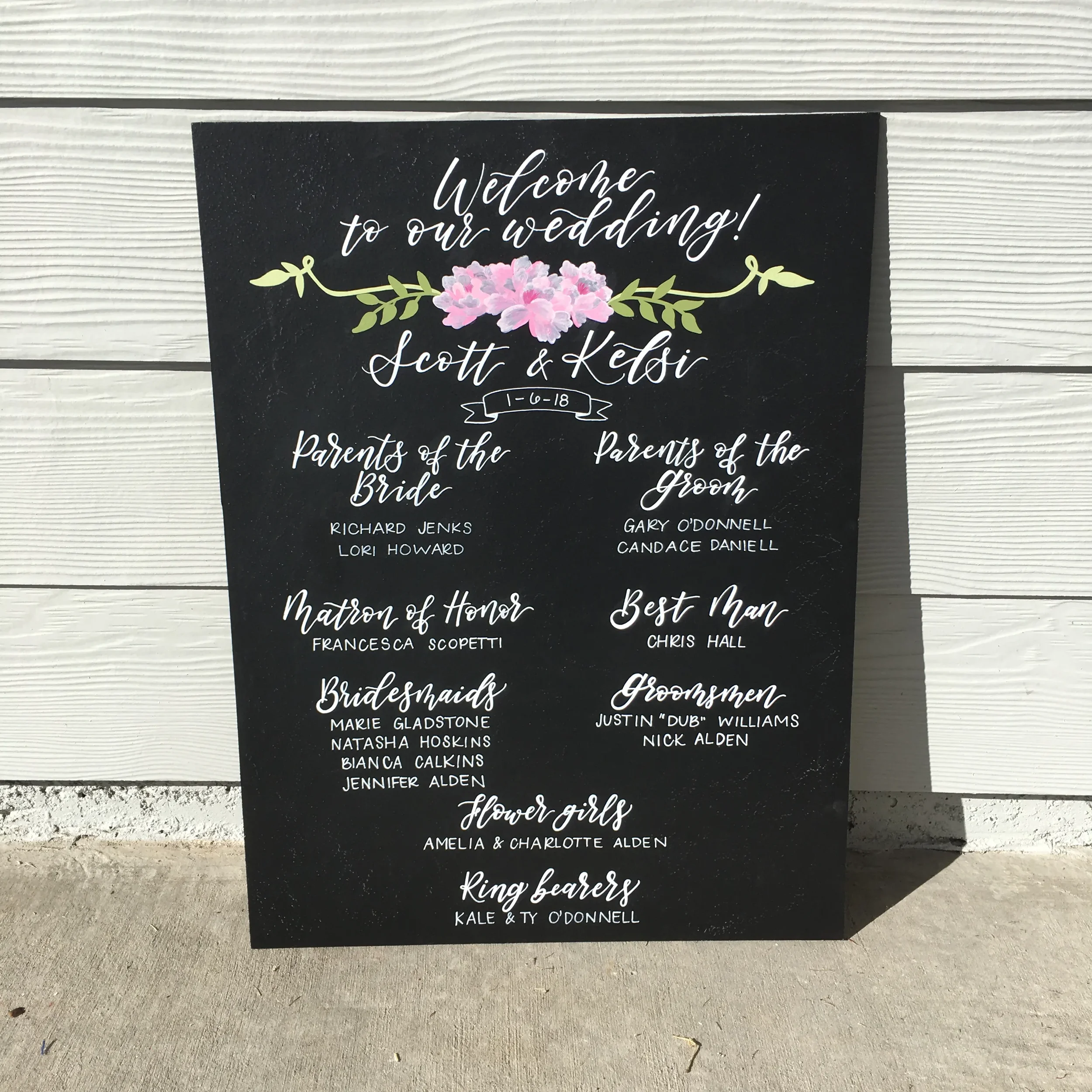 Custom hand-lettered chalkboard sign displaying parents of the bride, groom, and wedding party members.