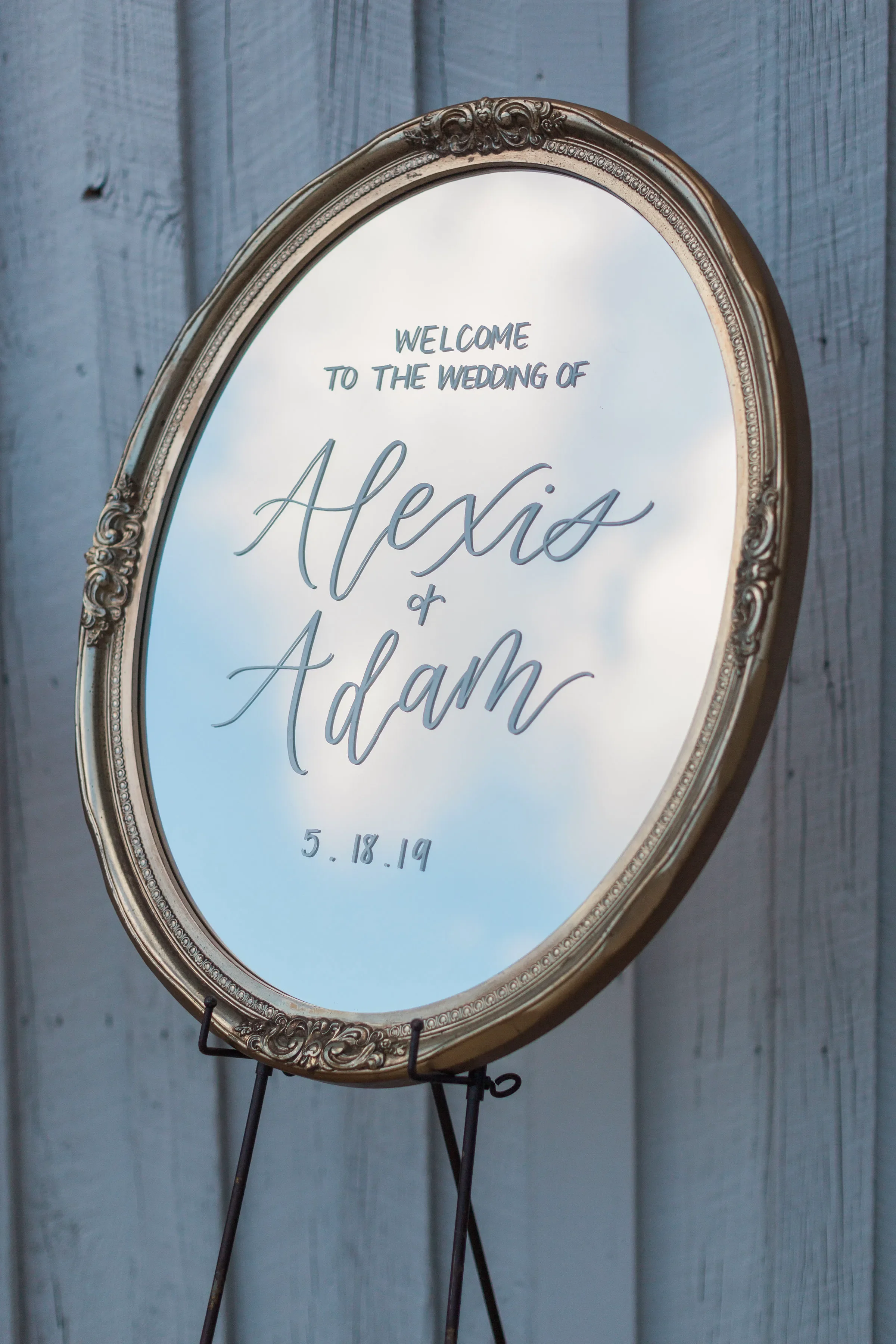 A large vintage gold oval framed mirror used as a wedding welcome sign with white script calligraphy displayed outdoors for a Georgia wedding.