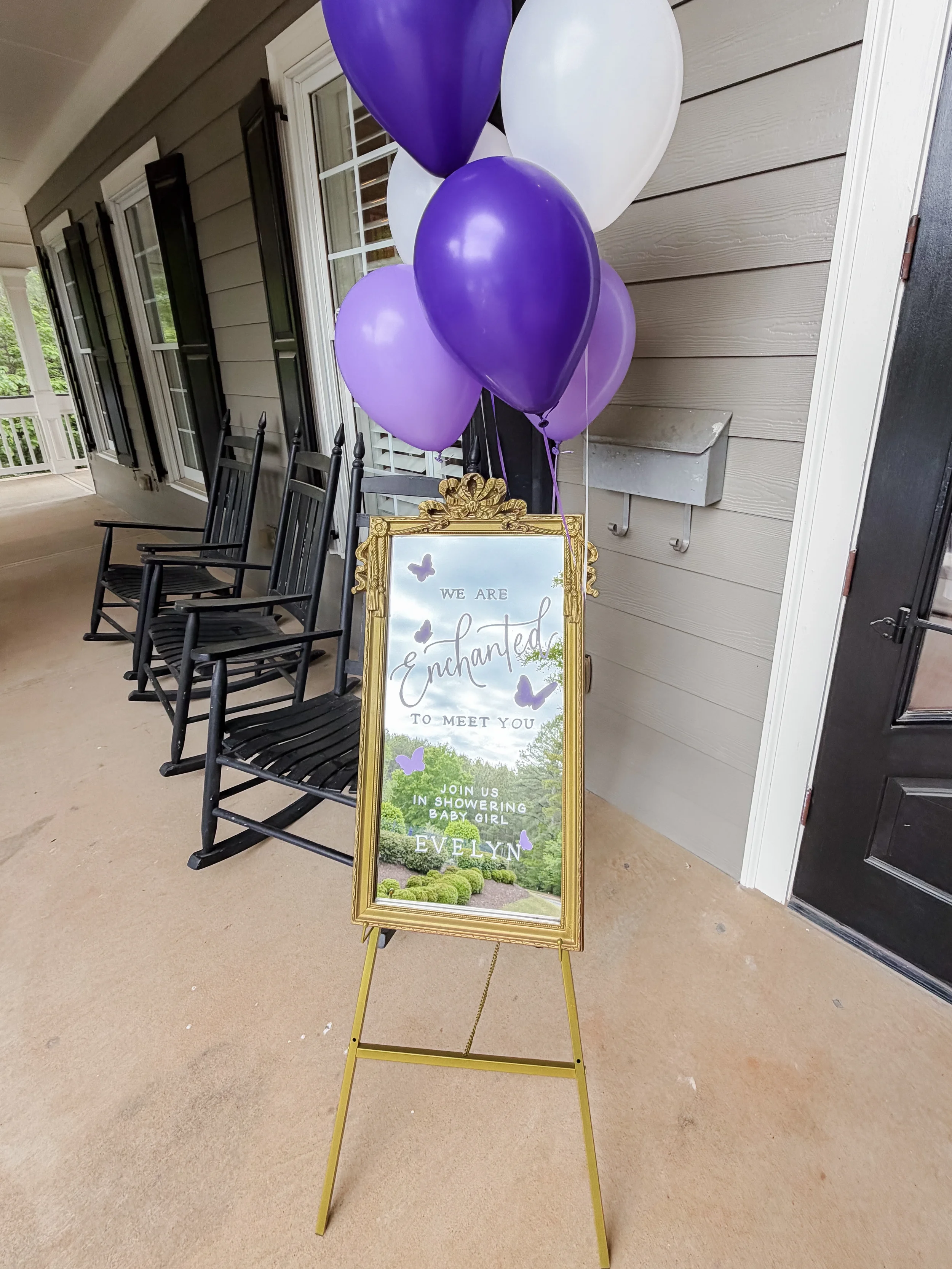 Vintage ornate gold mirror with purple calligraphed text reading "We Are Enchanted To Meet You" for Evelyn's baby shower welcome display.