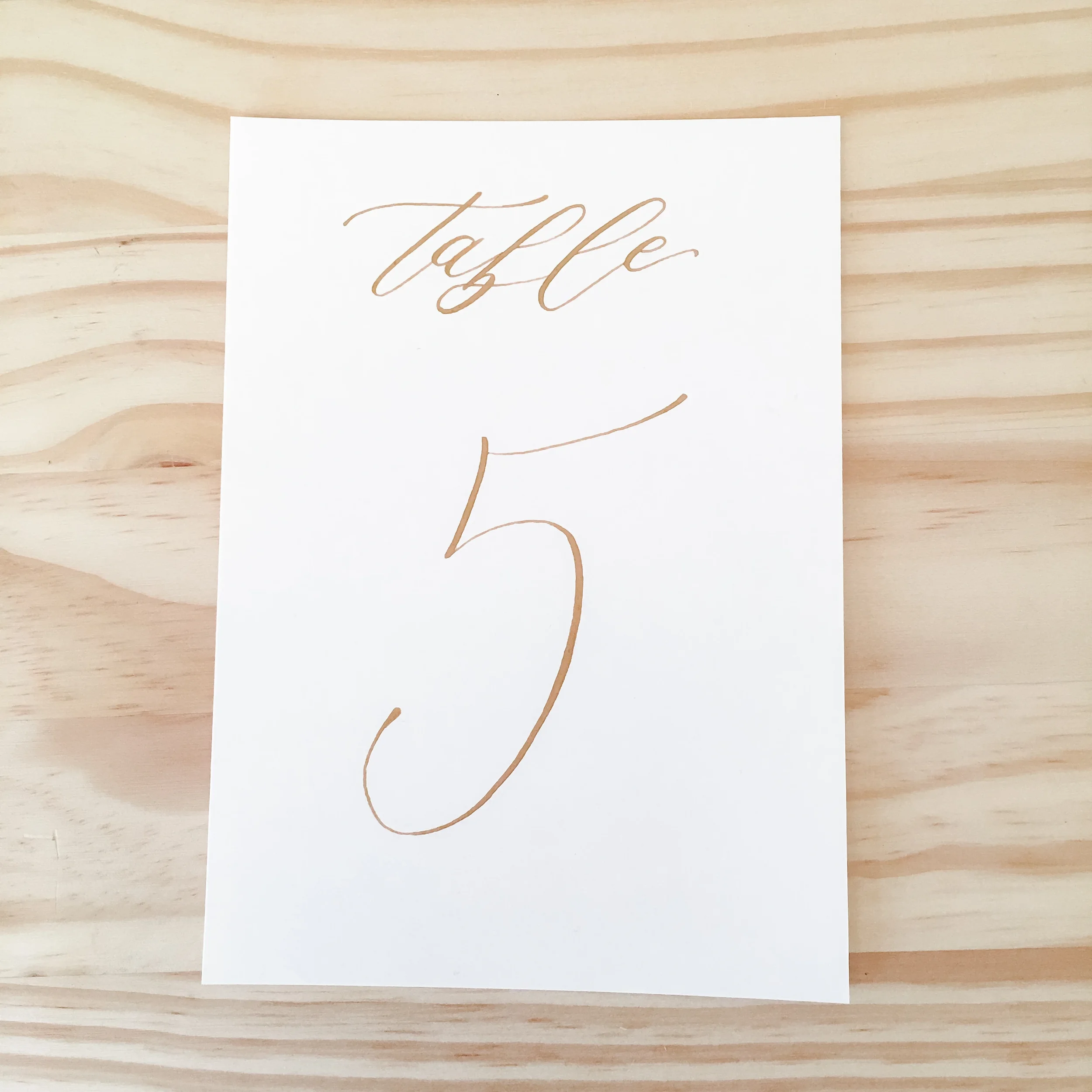 Gold calligraphy table numbers on white cardstock paper.