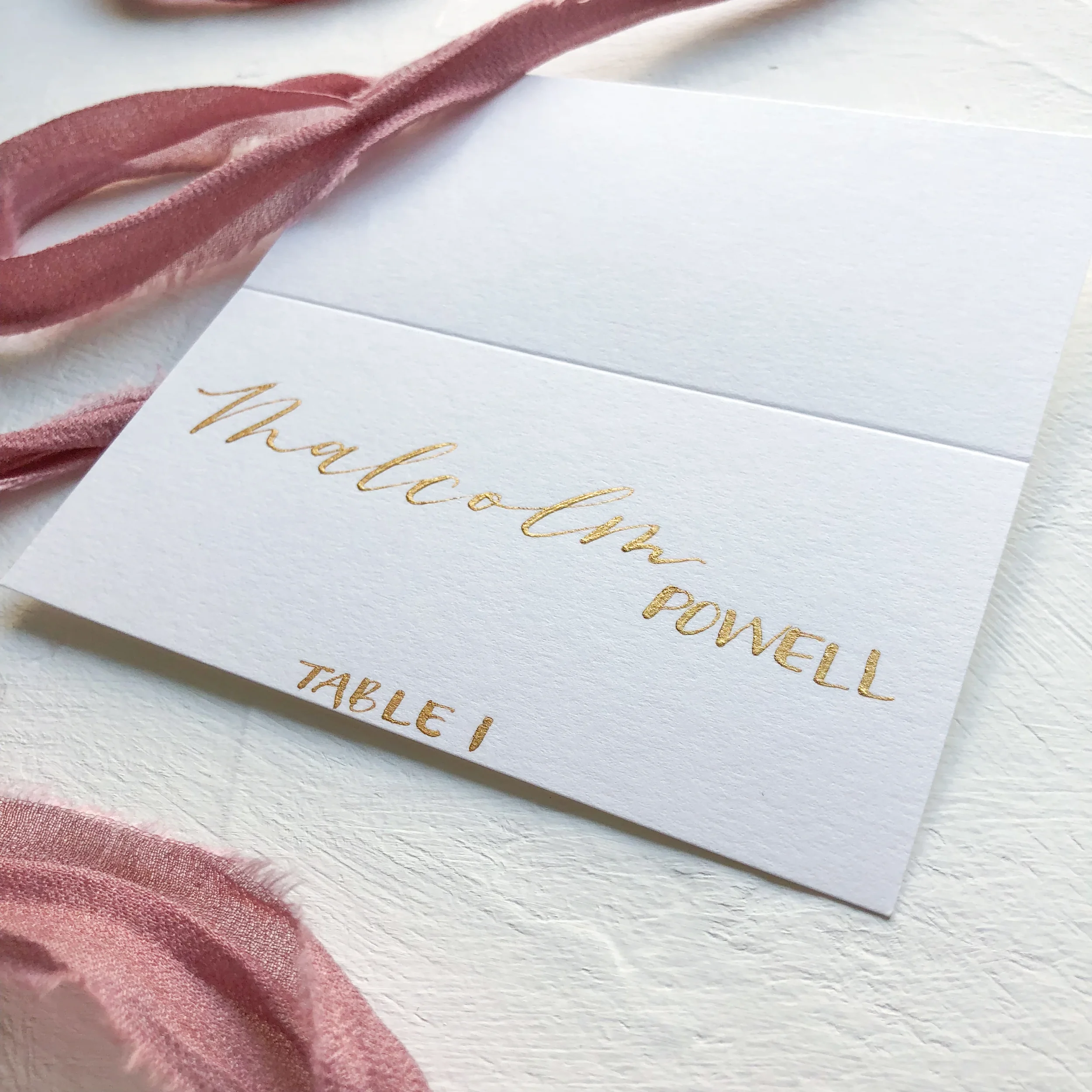 Add warm metallic shine to your guest arrival board with custom white paper escort cards lettered in metallic gold script.