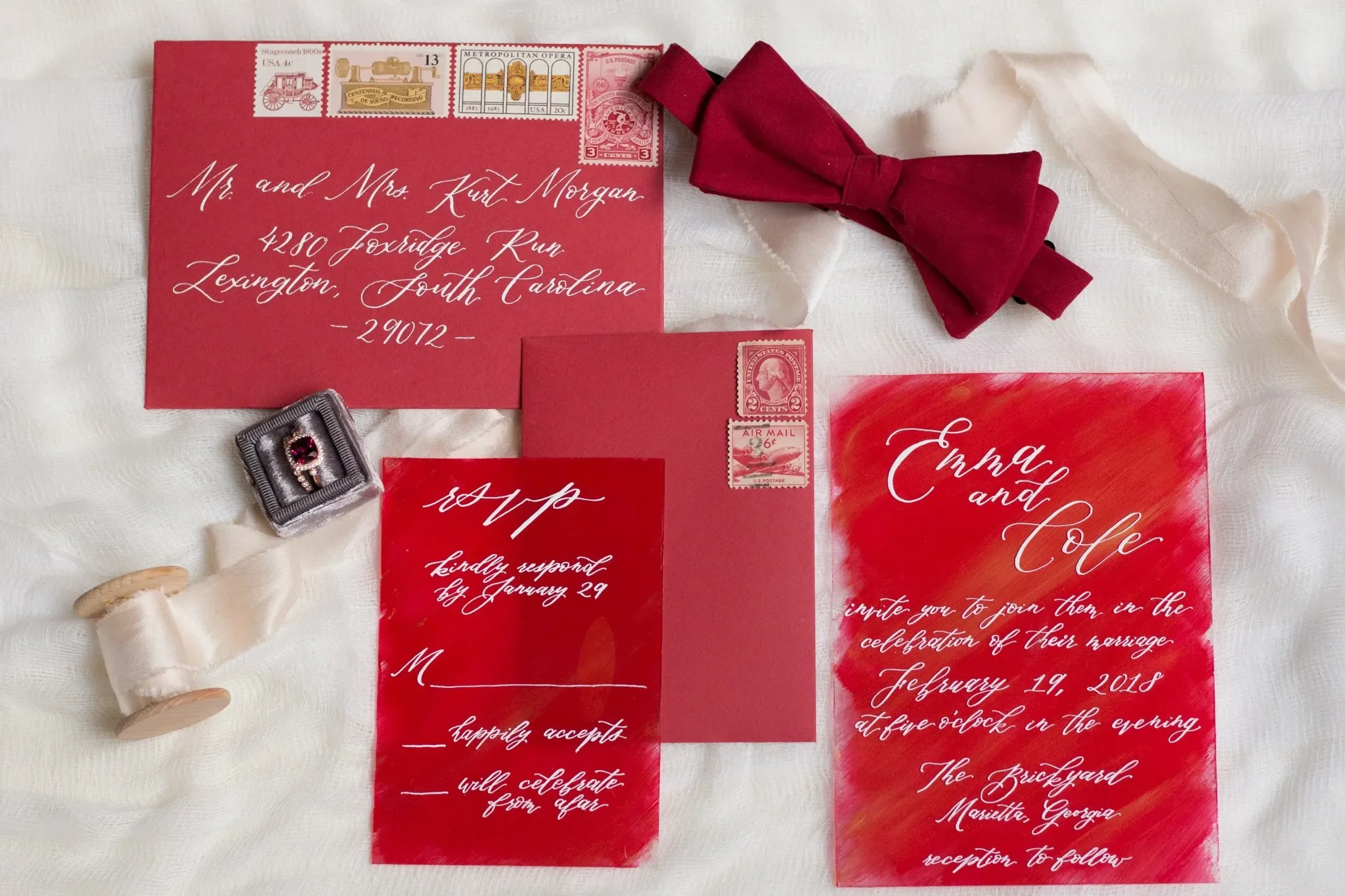 Bold crimson red acrylic wedding invitation with white calligraphy, paired with a matching burgundy velvet bow tie.