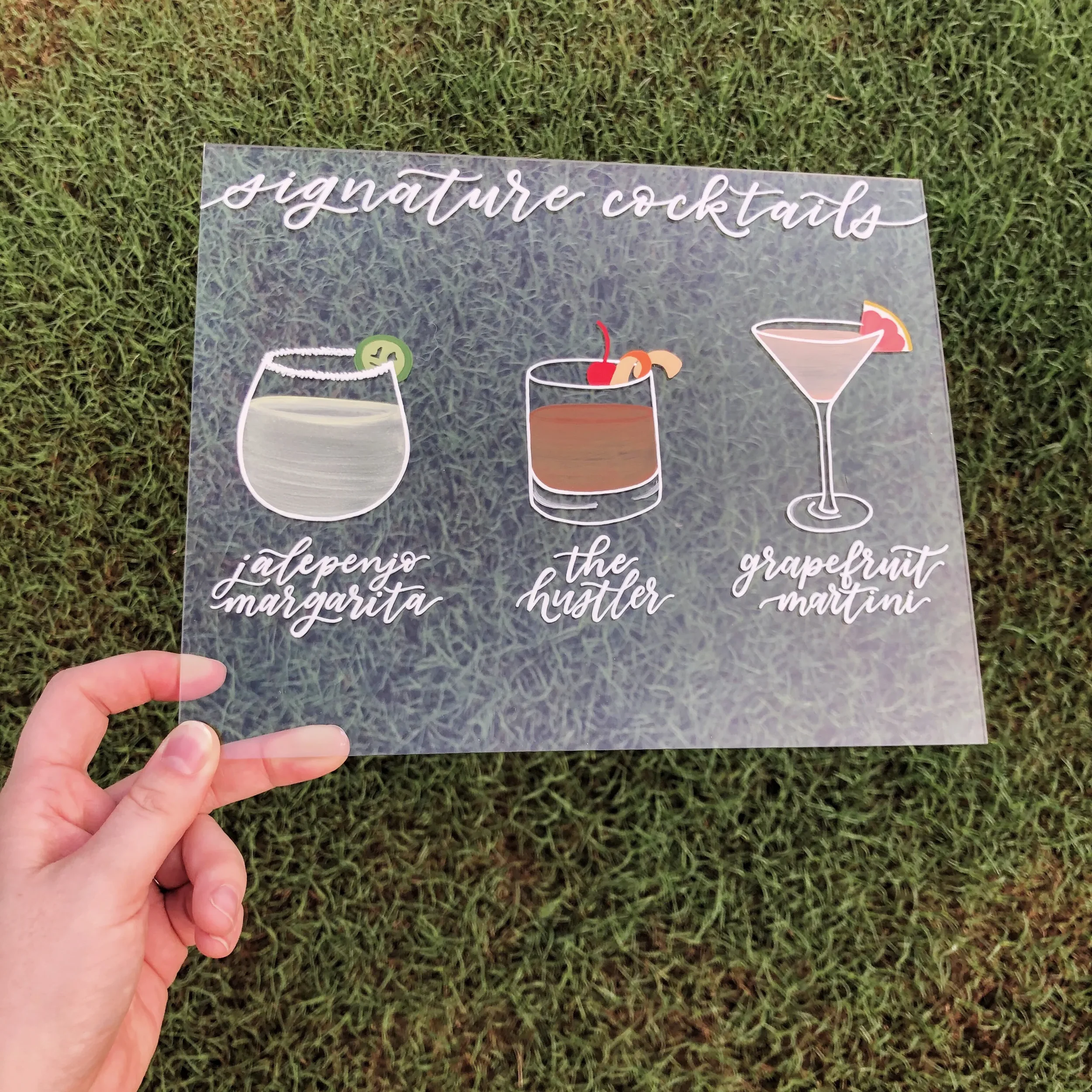 Showcase your favorite custom drinks with an interactive clear acrylic signature cocktails sign. Blending classic white ink script lettering with beautifully colorful, hand-painted illustrations of your mixed drinks, this custom bar accessory serves 