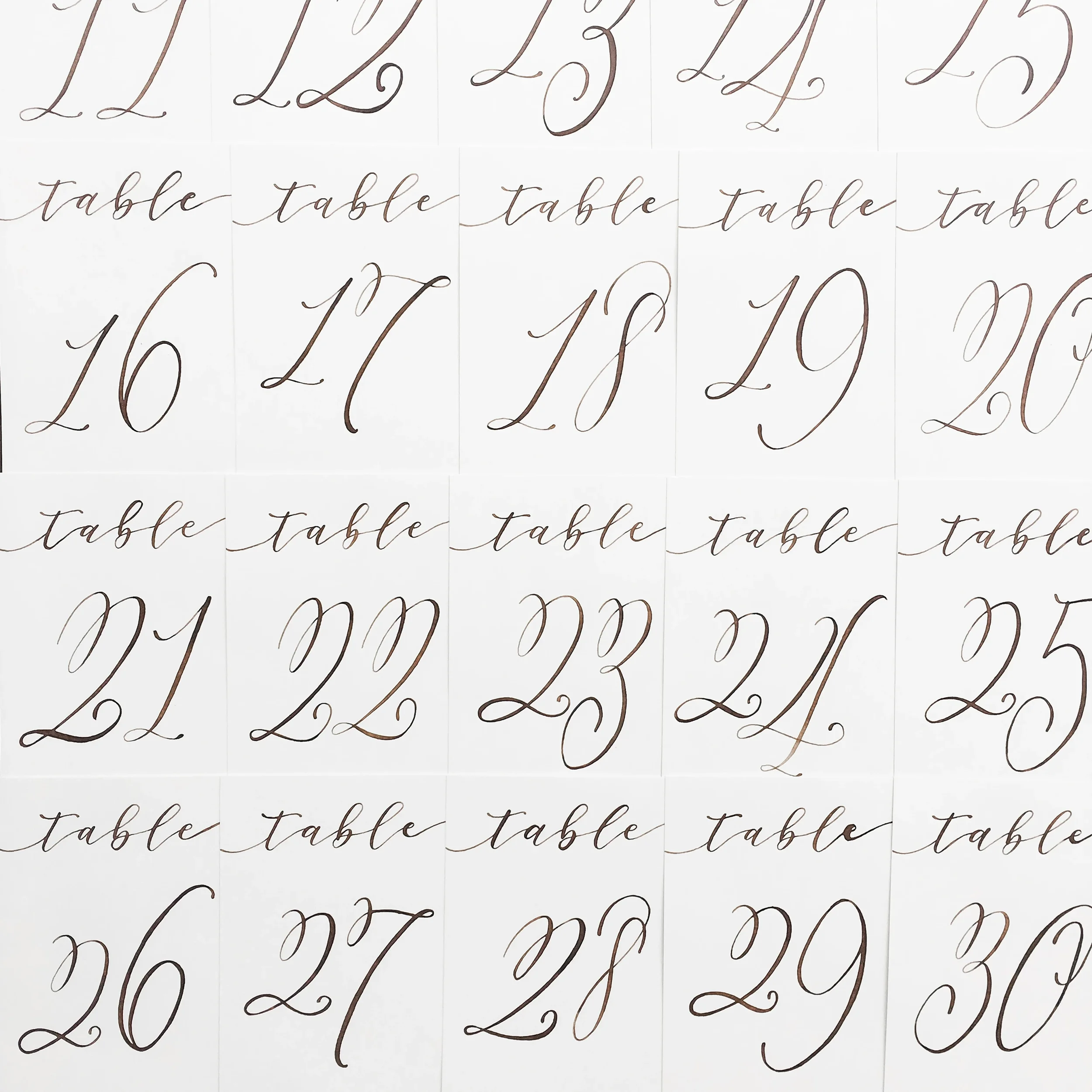Grid display of classic white paper table number cards with fine-line cursive script.