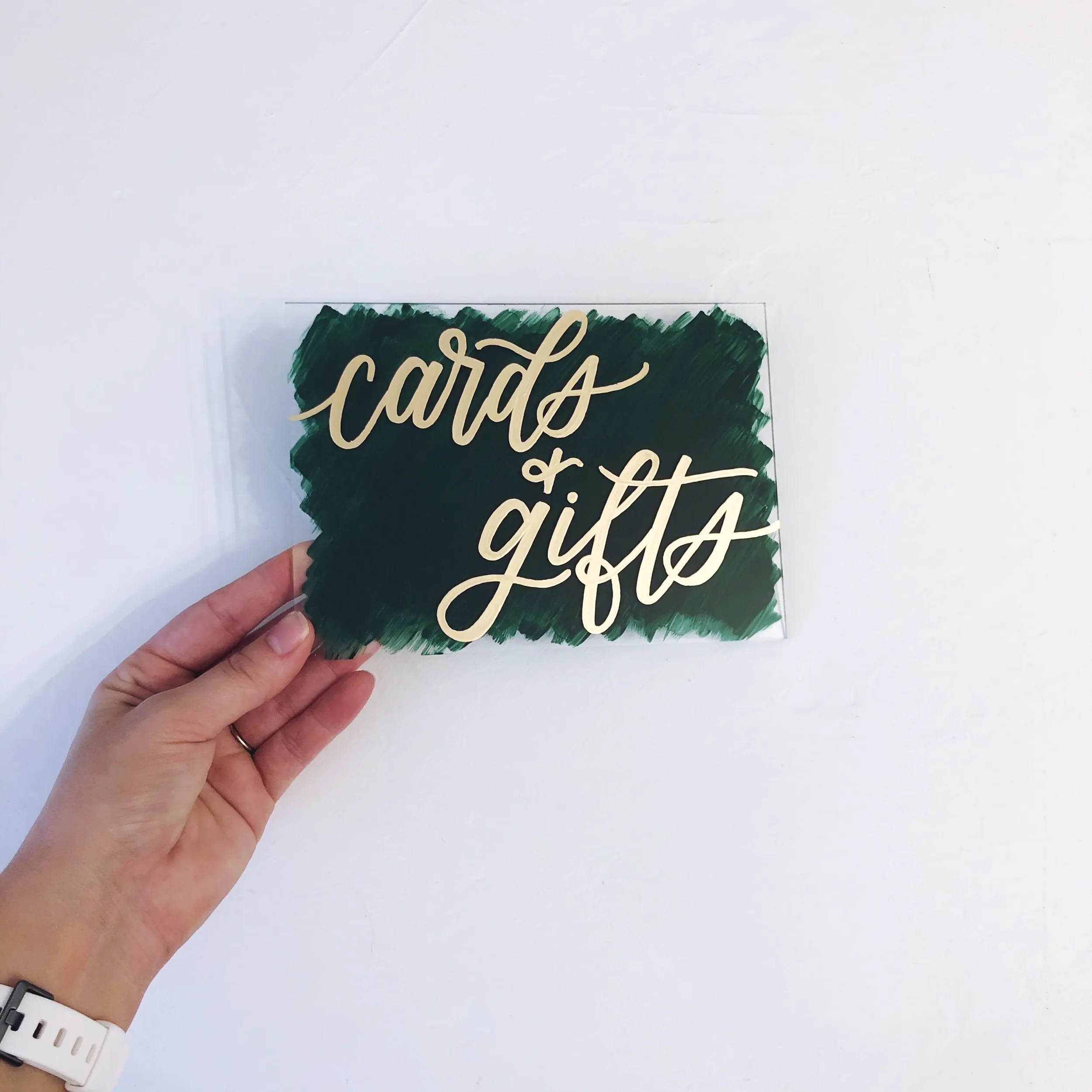 Small emerald green painted-back acrylic cards and gifts sign with elegant gold script lettering.