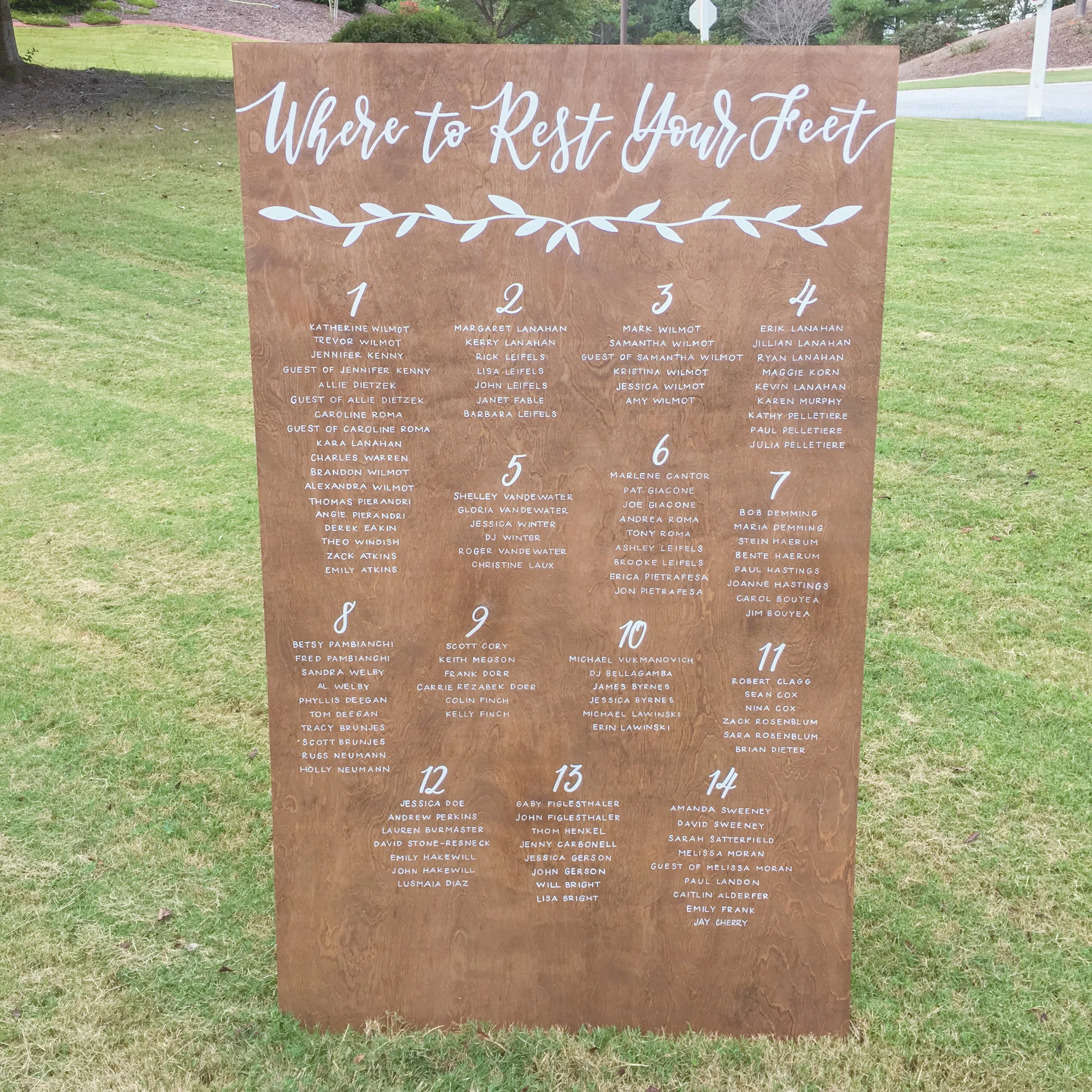 Large stained wood wedding seating chart with "where to rest your feet" at the top with hand painted greenery.