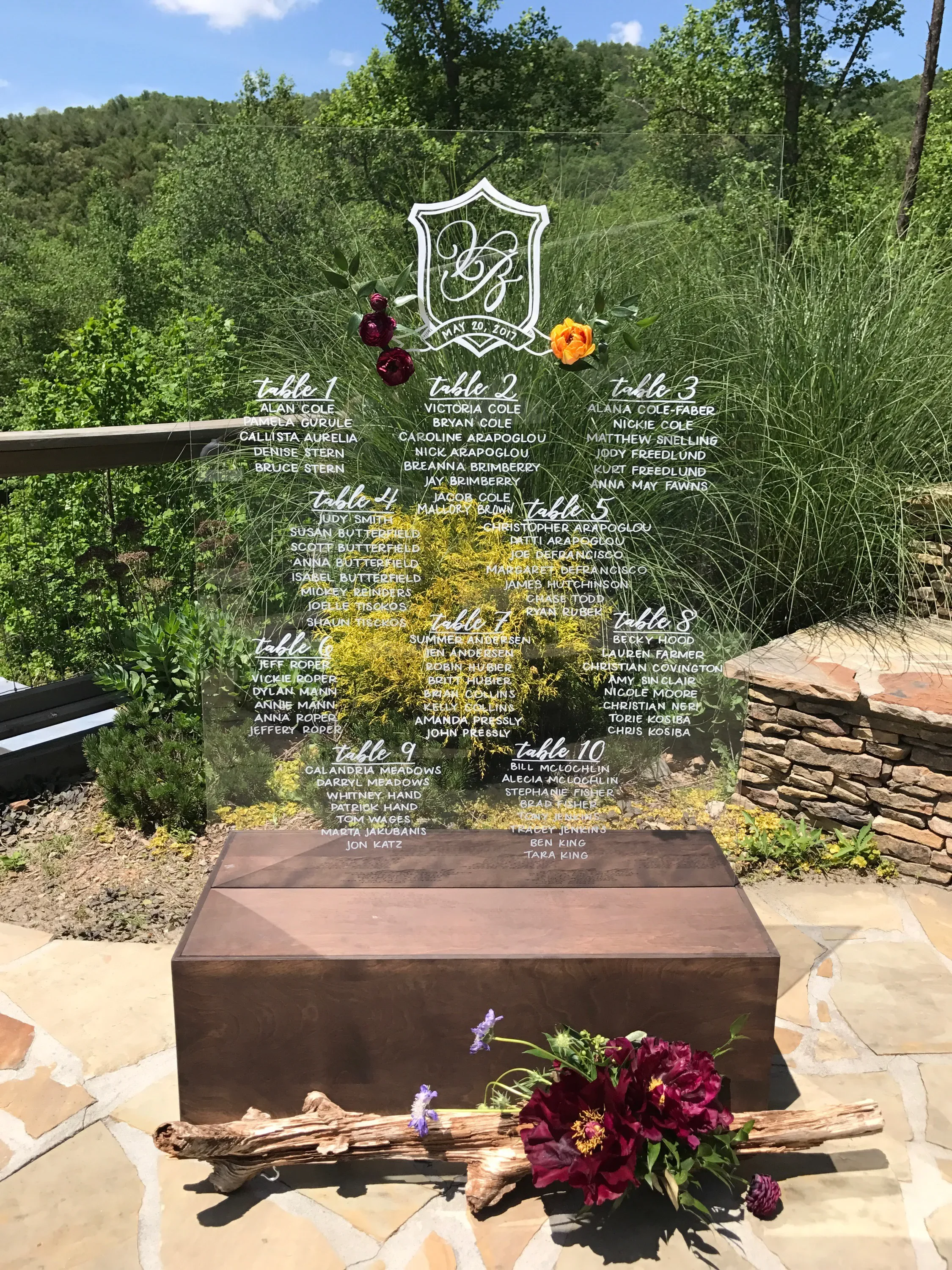 Outdoor acrylic wedding seating assignment sign decorated with deep burgundy florals.