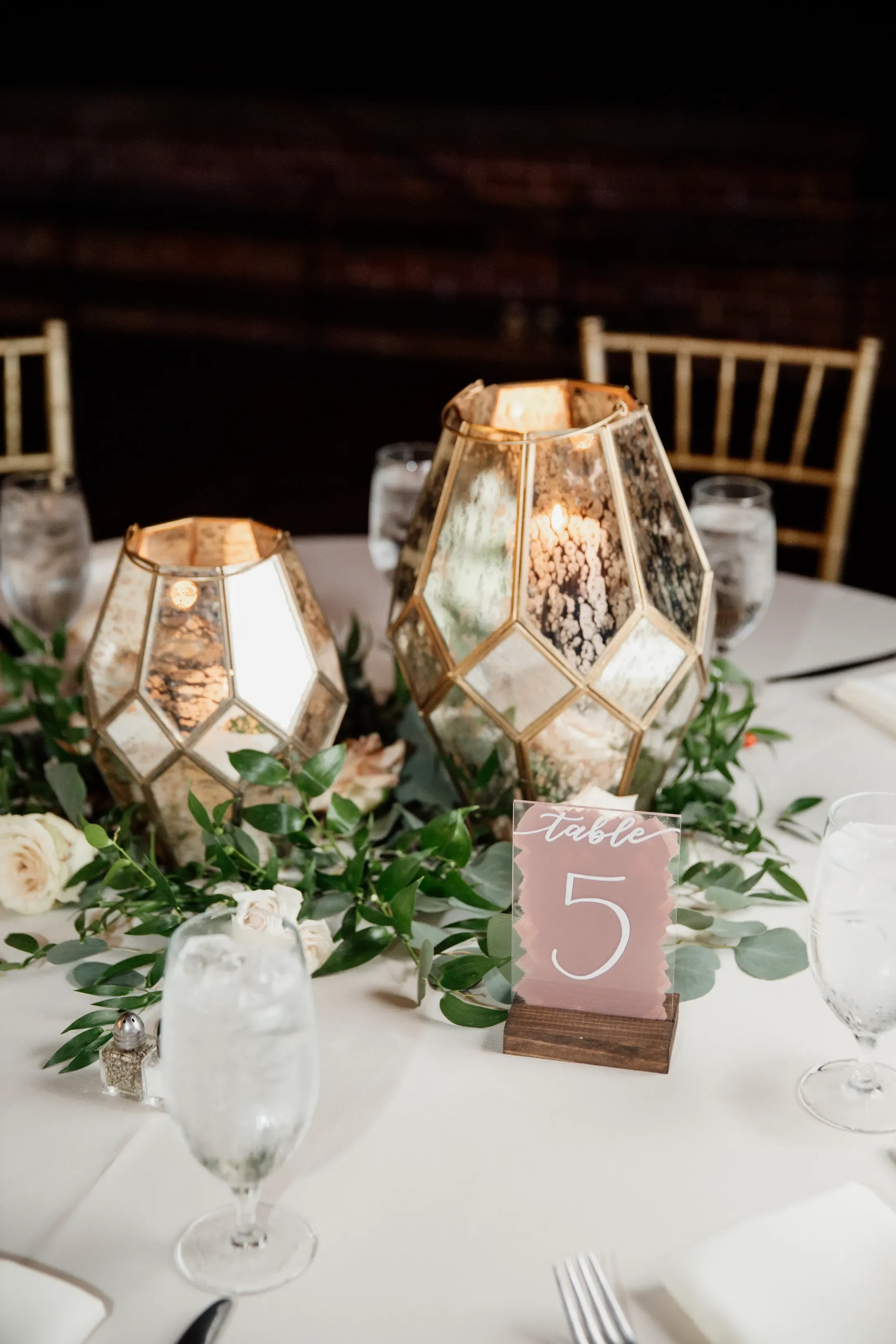 Modern custom acrylic table numbers featuring a rich, dusty mauve painted back and crisp white hand-lettered numbers, this signage design sits in a dark wooden block to beautifully complement romantic lush floral centerpieces and glowing candlelight.