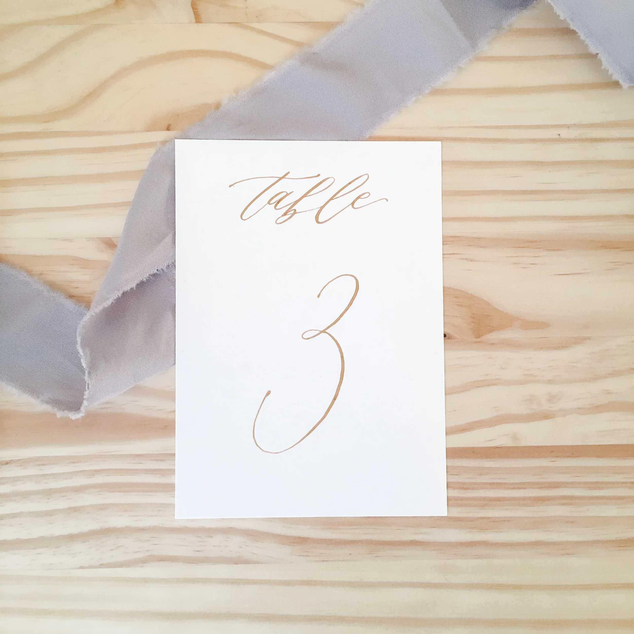 Classic white paper table number cards with fine-line cursive script in gold ink.