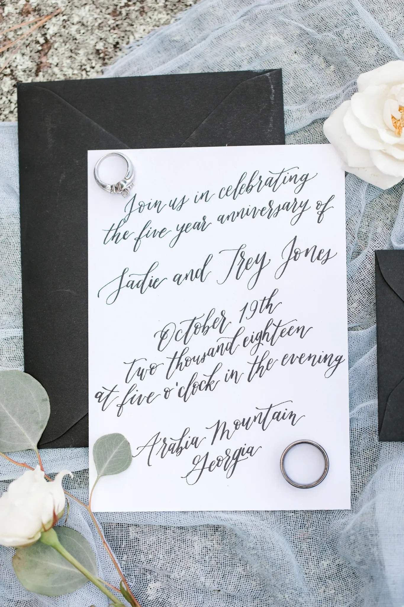 Classic black and white stationery design flat lay with custom cursive handwriting and accent greenery.