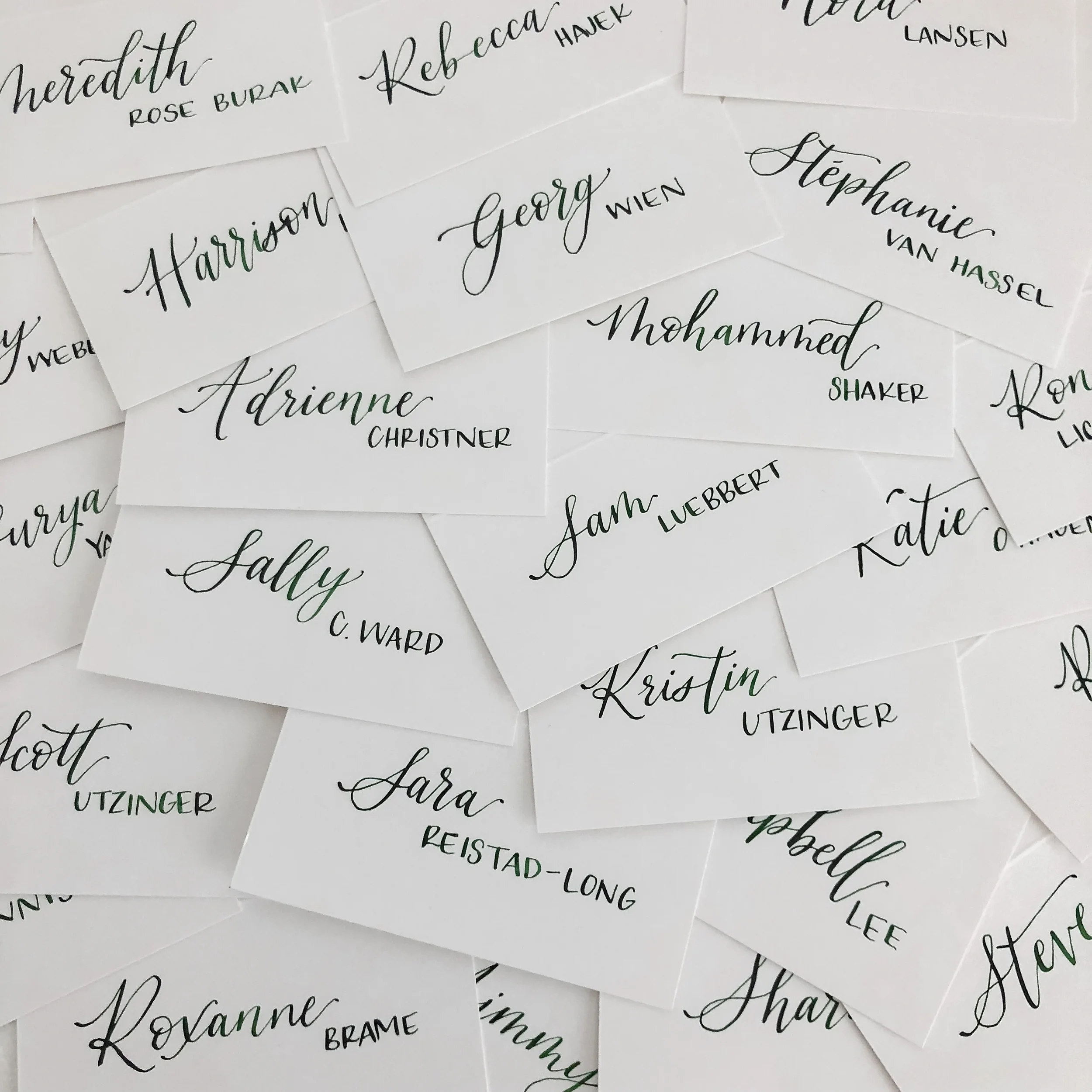 Mixed modern calligraphy place cards in dark green ink on white folded cards.