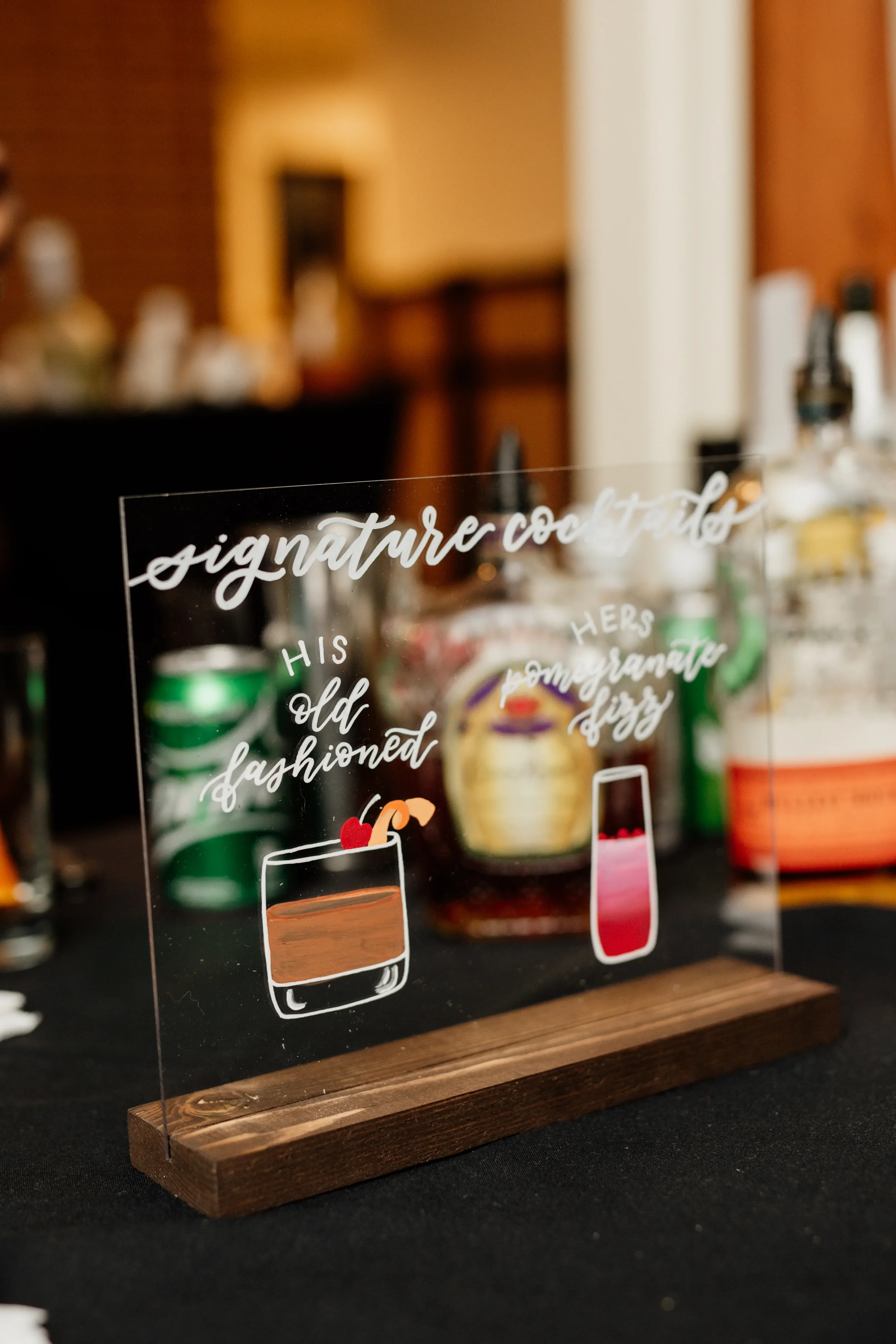 Hand-lettered clear acrylic signature cocktail bar sign with painted drink illustrations.