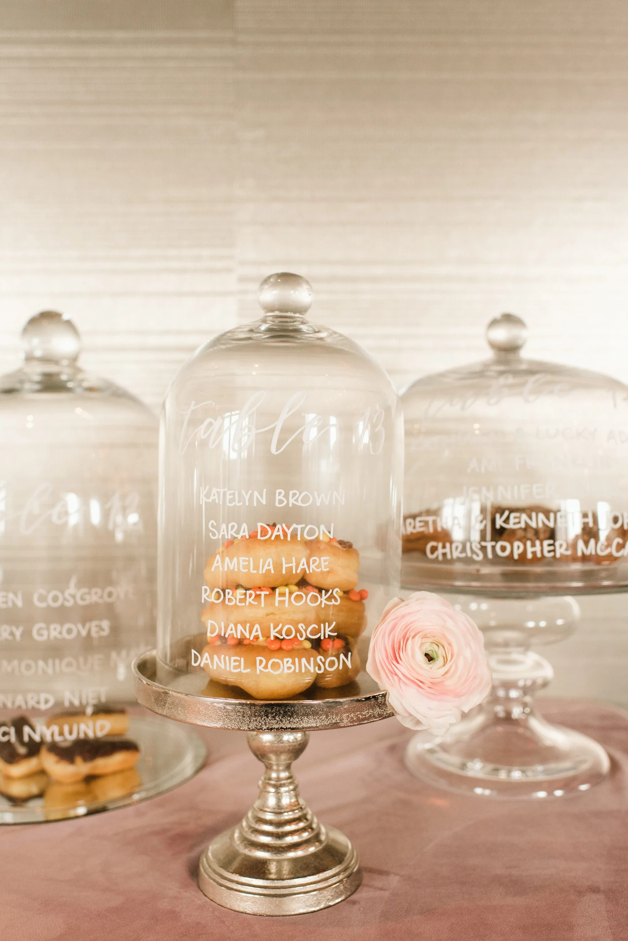 Infuse interactive creativity into your reception styling with a glass cloche seating display. Combining delicious treats with hidden table assignments beneath vintage glass domes, this playful presentation turns guest coordination into a delightful 