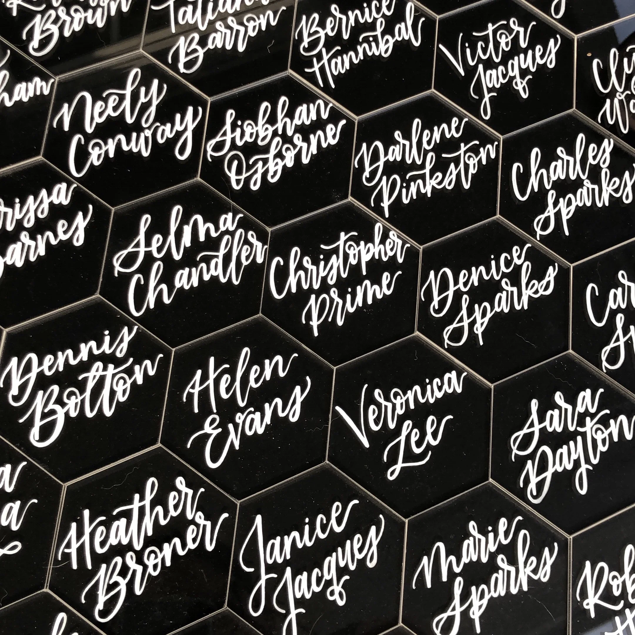 Black acrylic hexagon place cards with white hand lettered names for a modern wedding table setting.