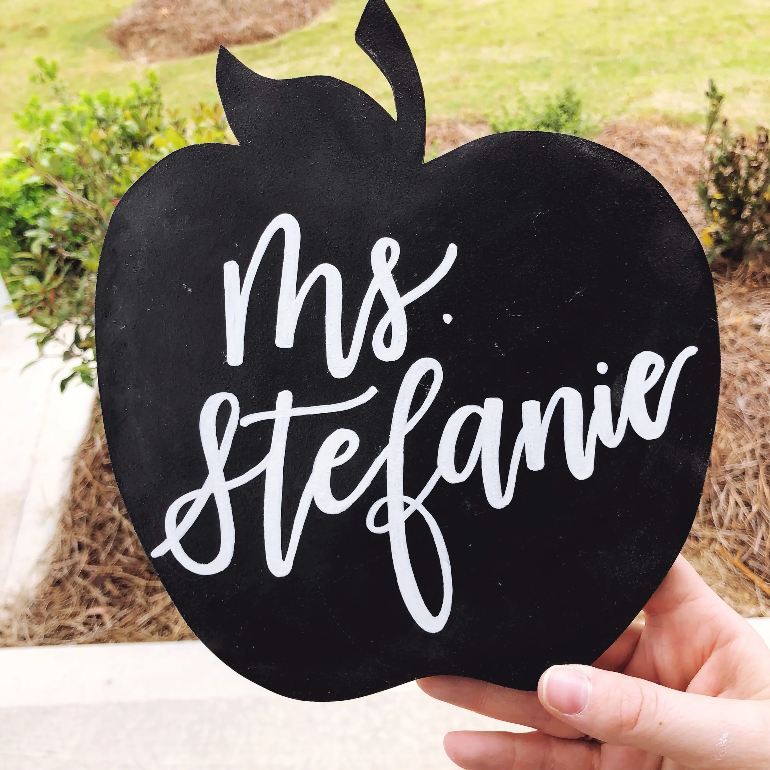Looking for a timeless back-to-school or teacher appreciation gift? This custom apple-shaped chalkboard desk sign is hand-lettered with flawless white script calligraphy. Mounted on a minimalist natural wood base, it serves as a charming classroom we