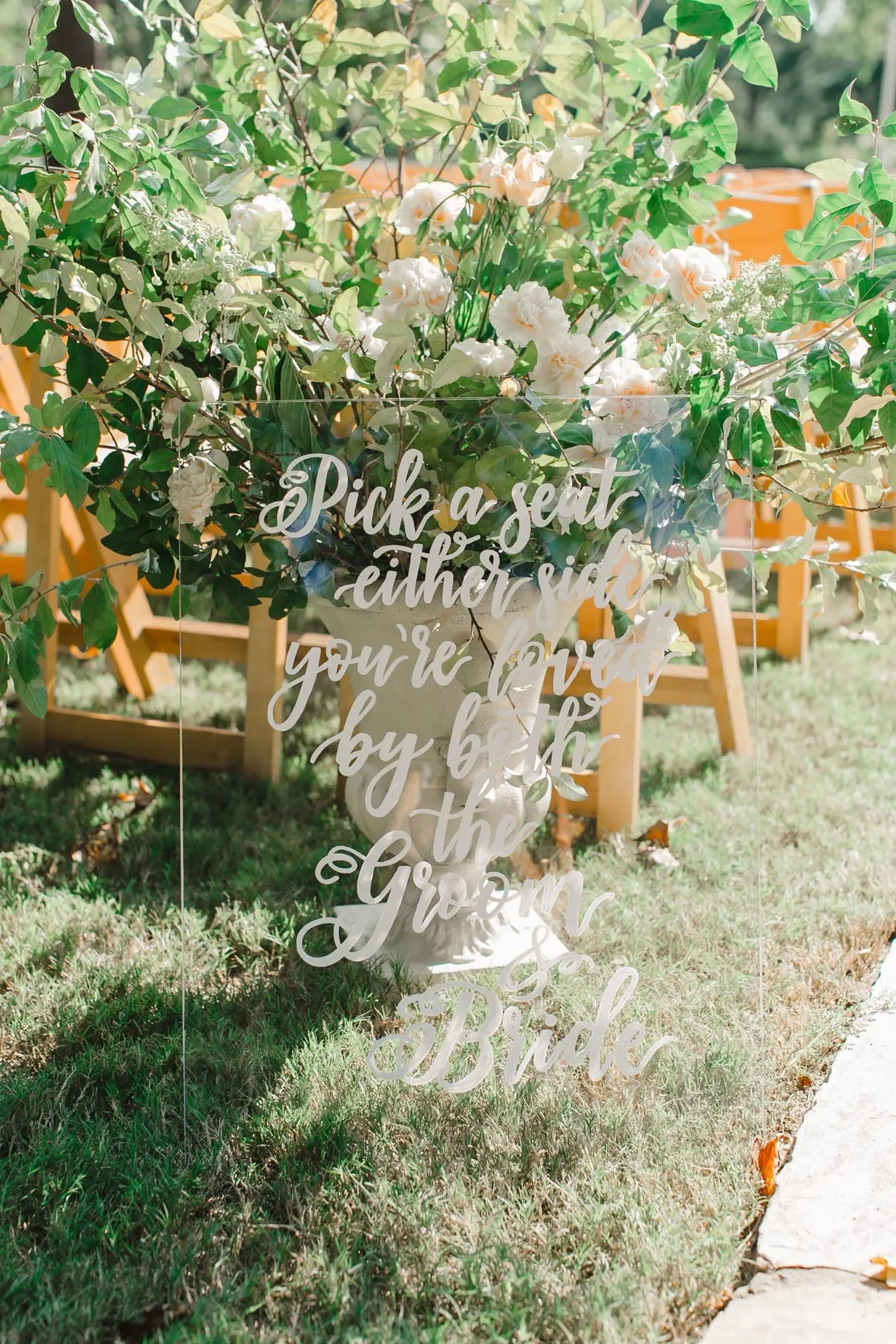 Custom clear acrylic wedding ceremony sign saying "pick a seat not a side" in white script calligraphy.
