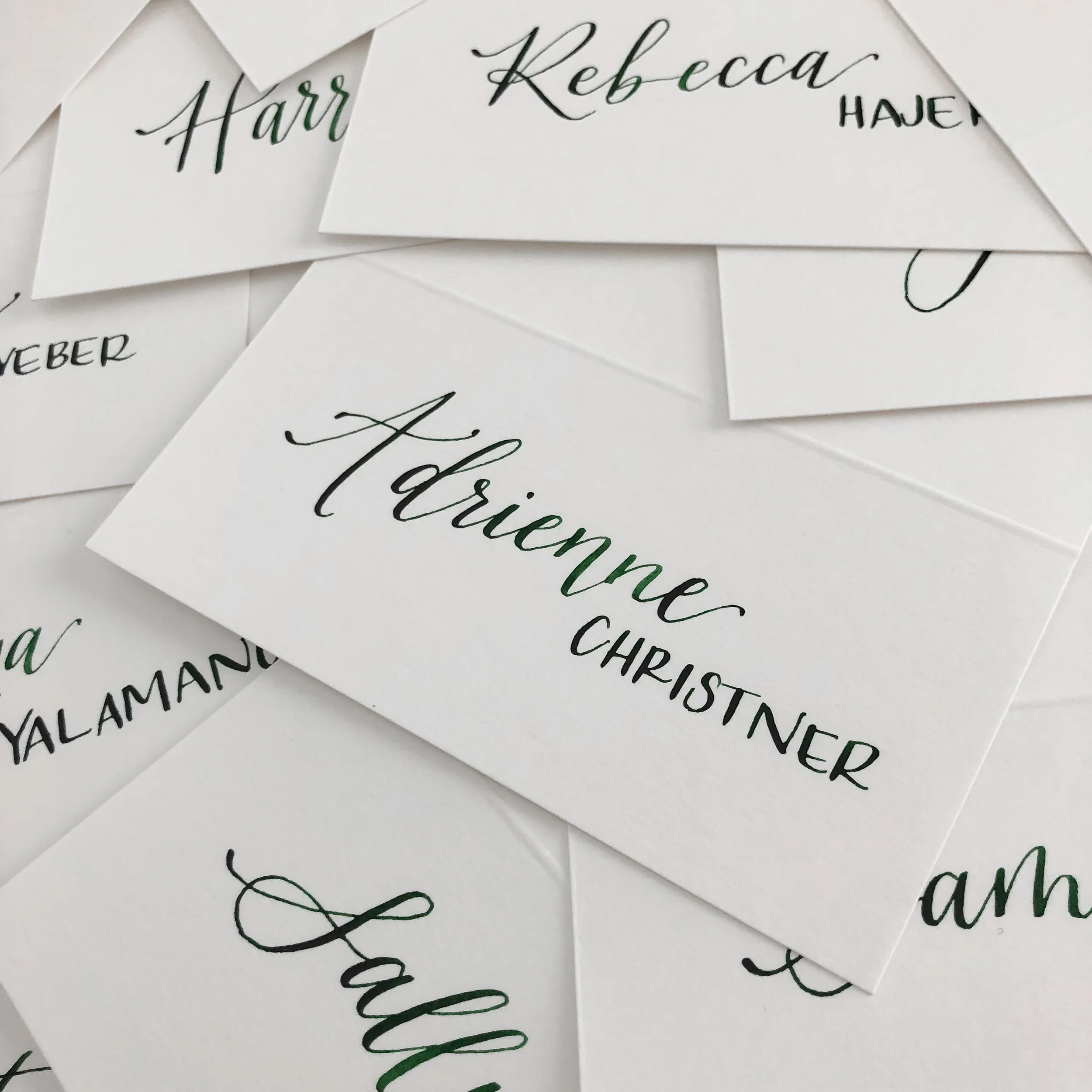 Mixed modern calligraphy place cards in dark green ink on white folded cards.