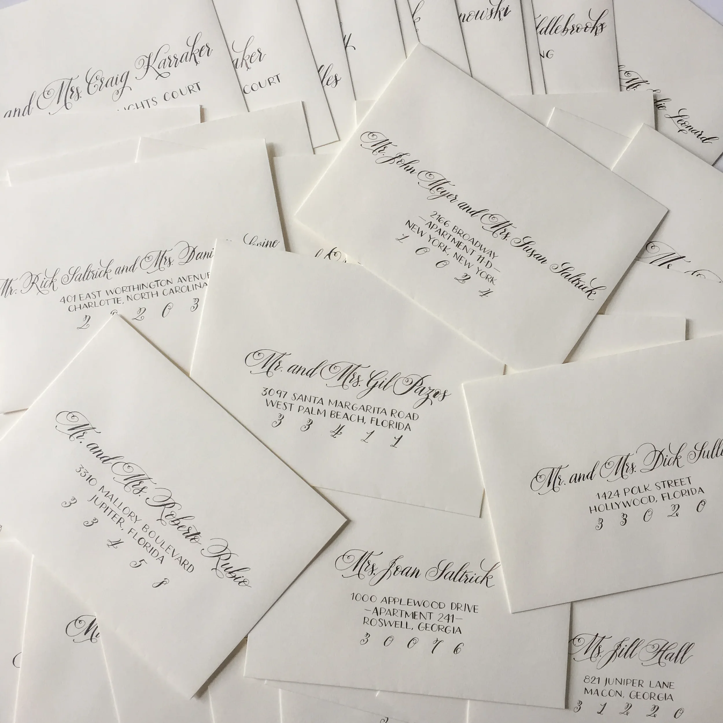 A large scattered stack of off-white wedding envelopes hand-addressed in crisp black script calligraphy.