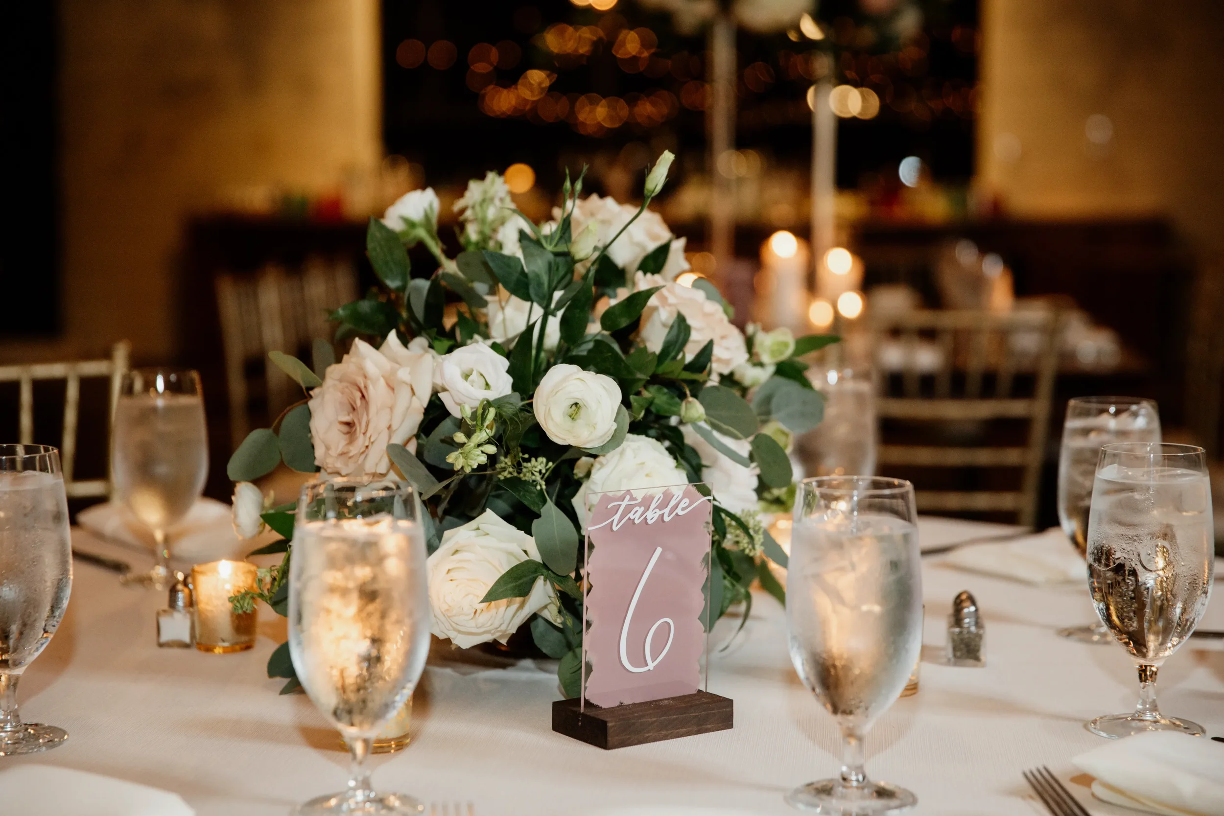 Mauve painted back acrylic wedding table number sign with a dark wood stand.