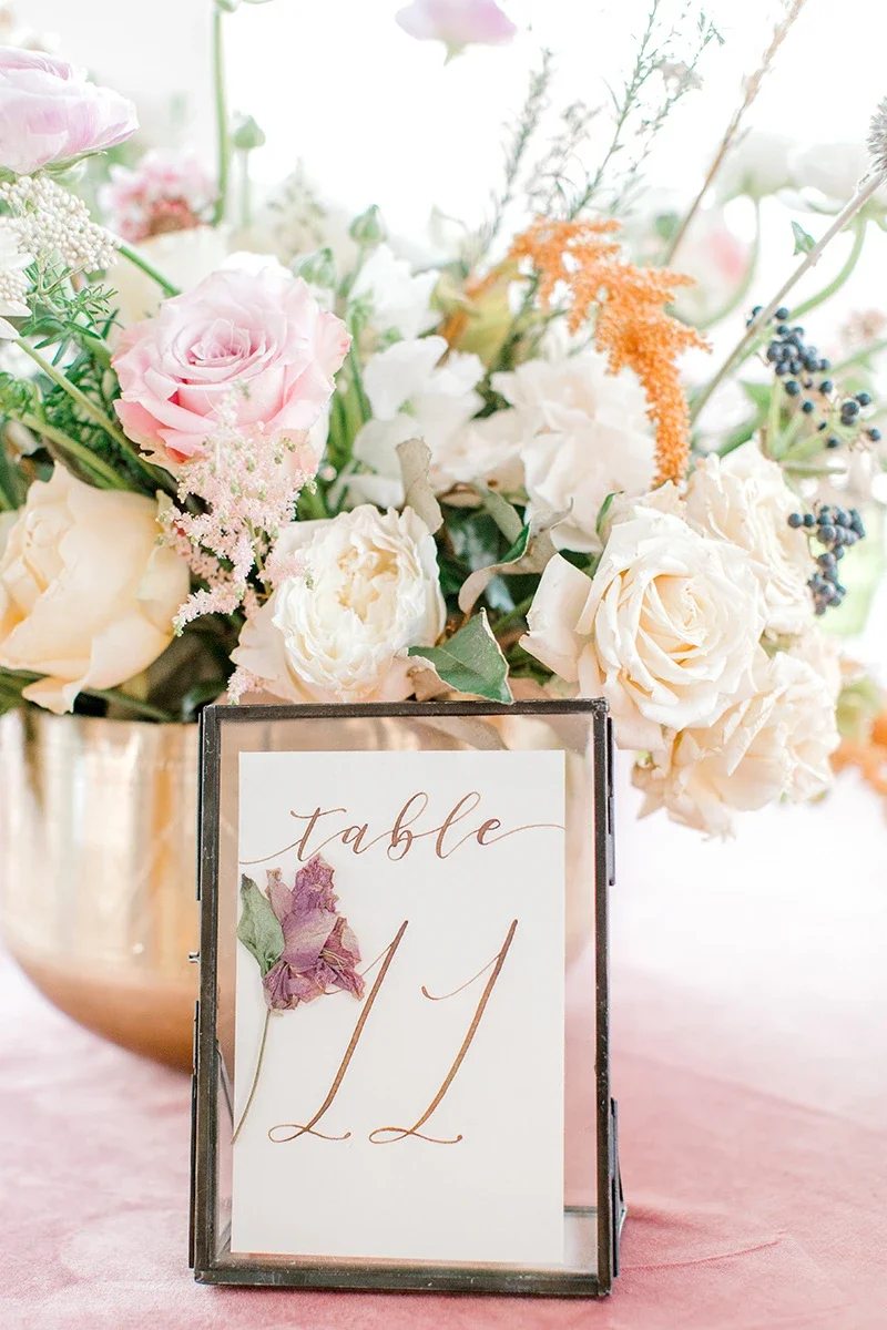 Glass floating frame table number 3 with a pressed yellow flower and metallic gold script calligraphy.