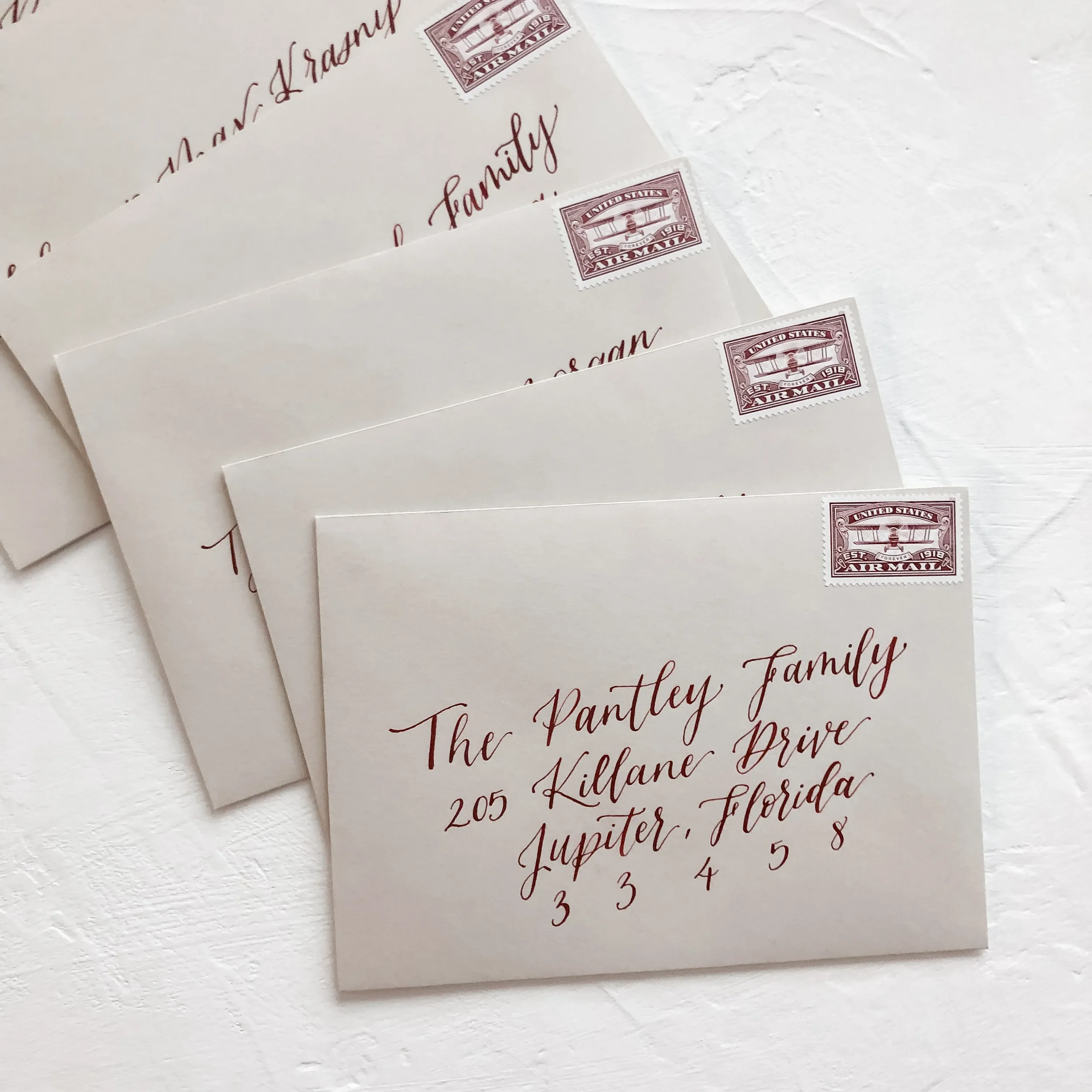 Stack of taupe kraft paper envelopes addressed in a deep burgundy calligraphy font with vintage stamps.
