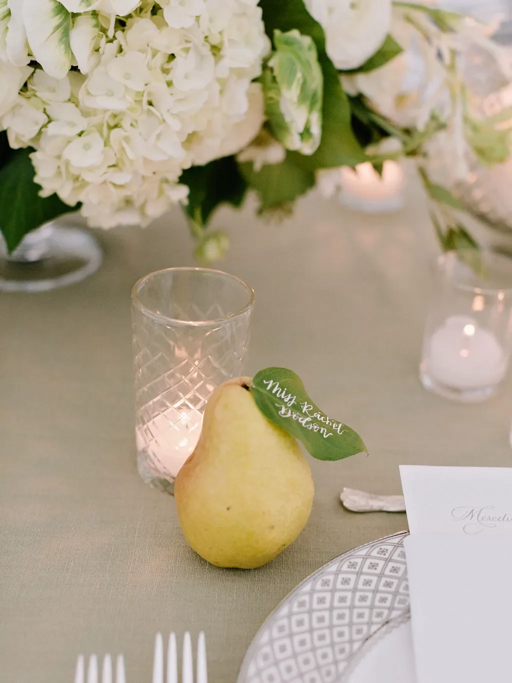 Hand-lettered pear escort card complements a romantic garden-inspired wedding tablescape featuring lush florals, candlelight, and timeless reception details.