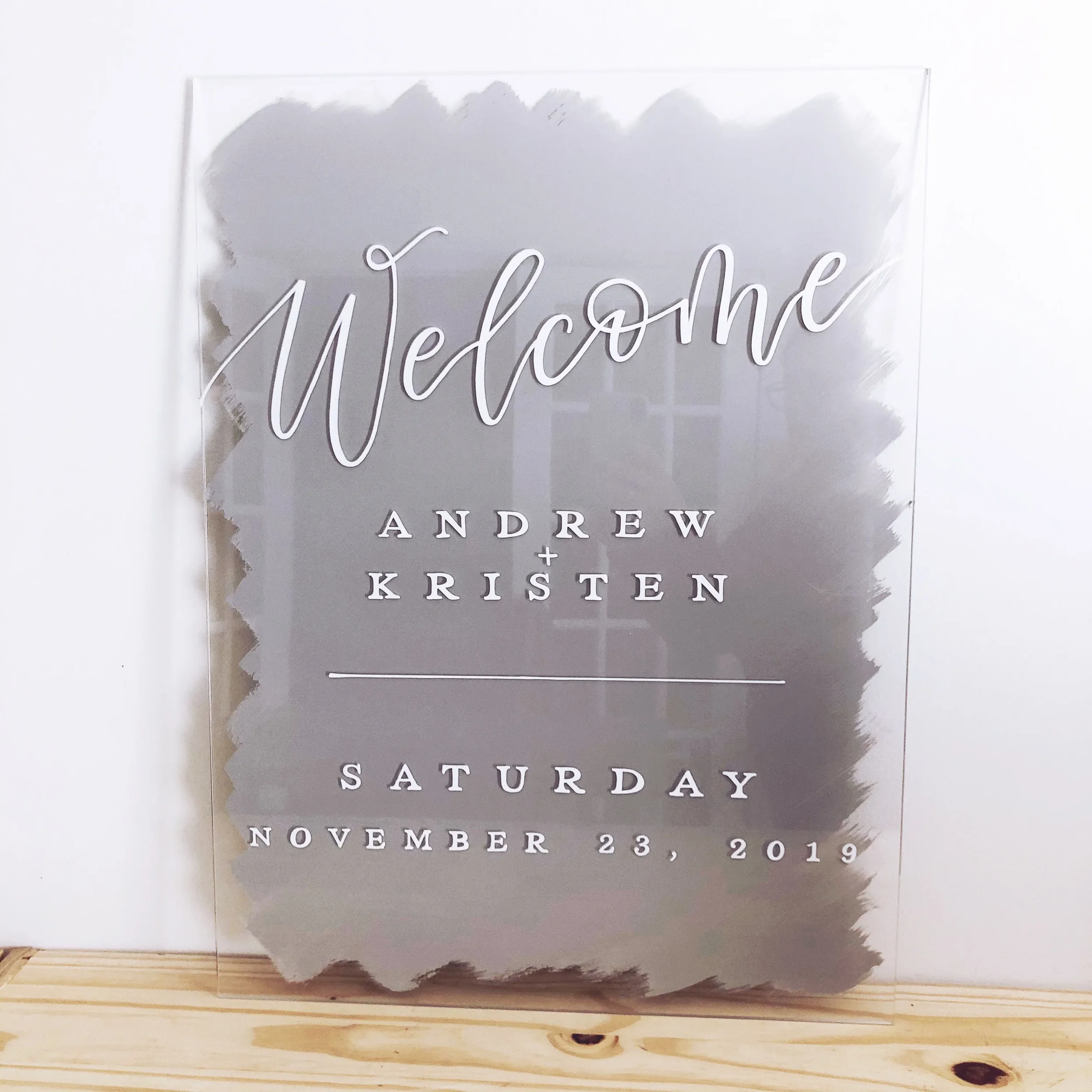 Frosted grey painted-back acrylic wedding welcome sign with fine white hand-lettered calligraphy.