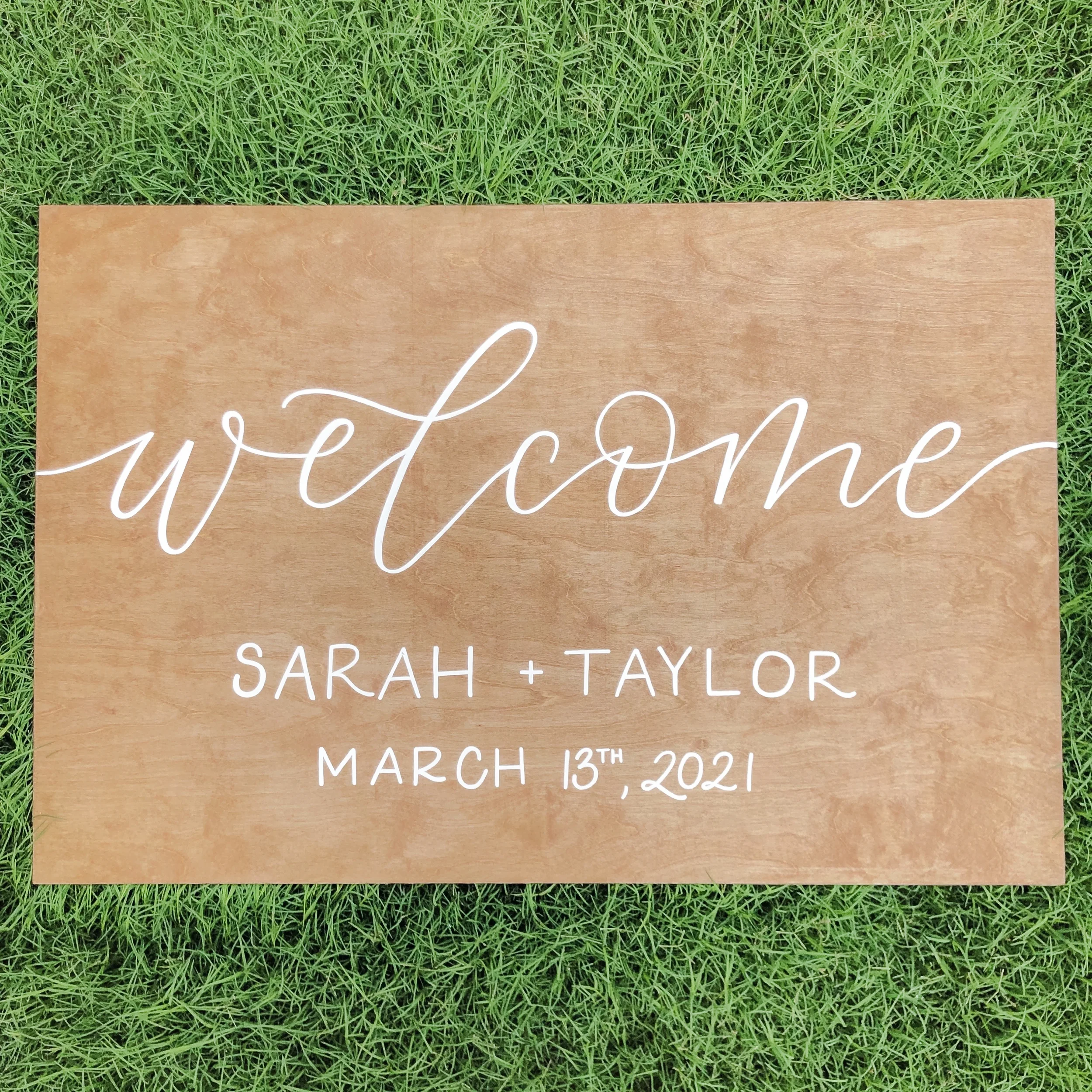 Wooden wedding welcome sign on grass featuring white script and block hand-lettering.