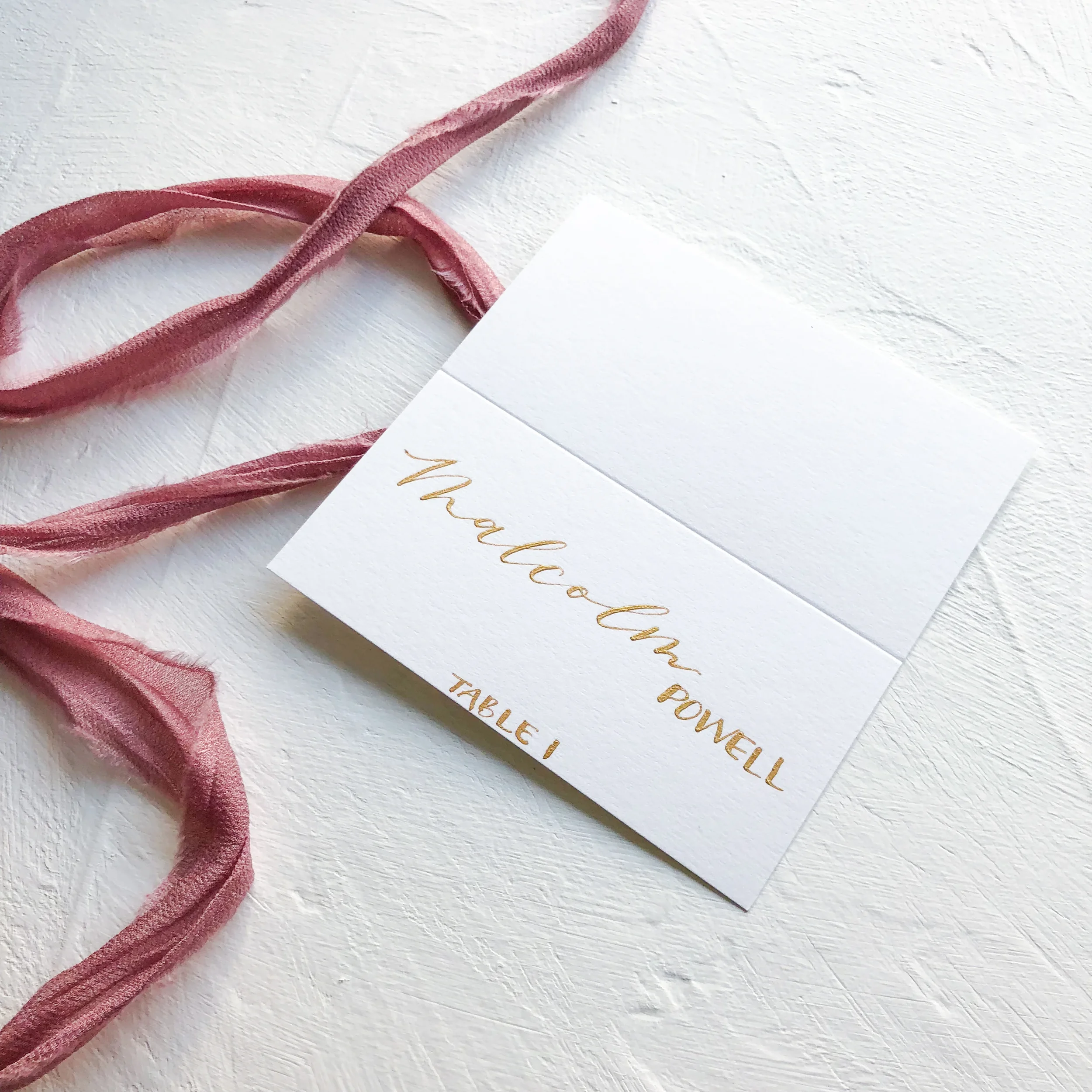 White wedding escort cards hand-lettered in metallic gold script calligraphy with table numbers.