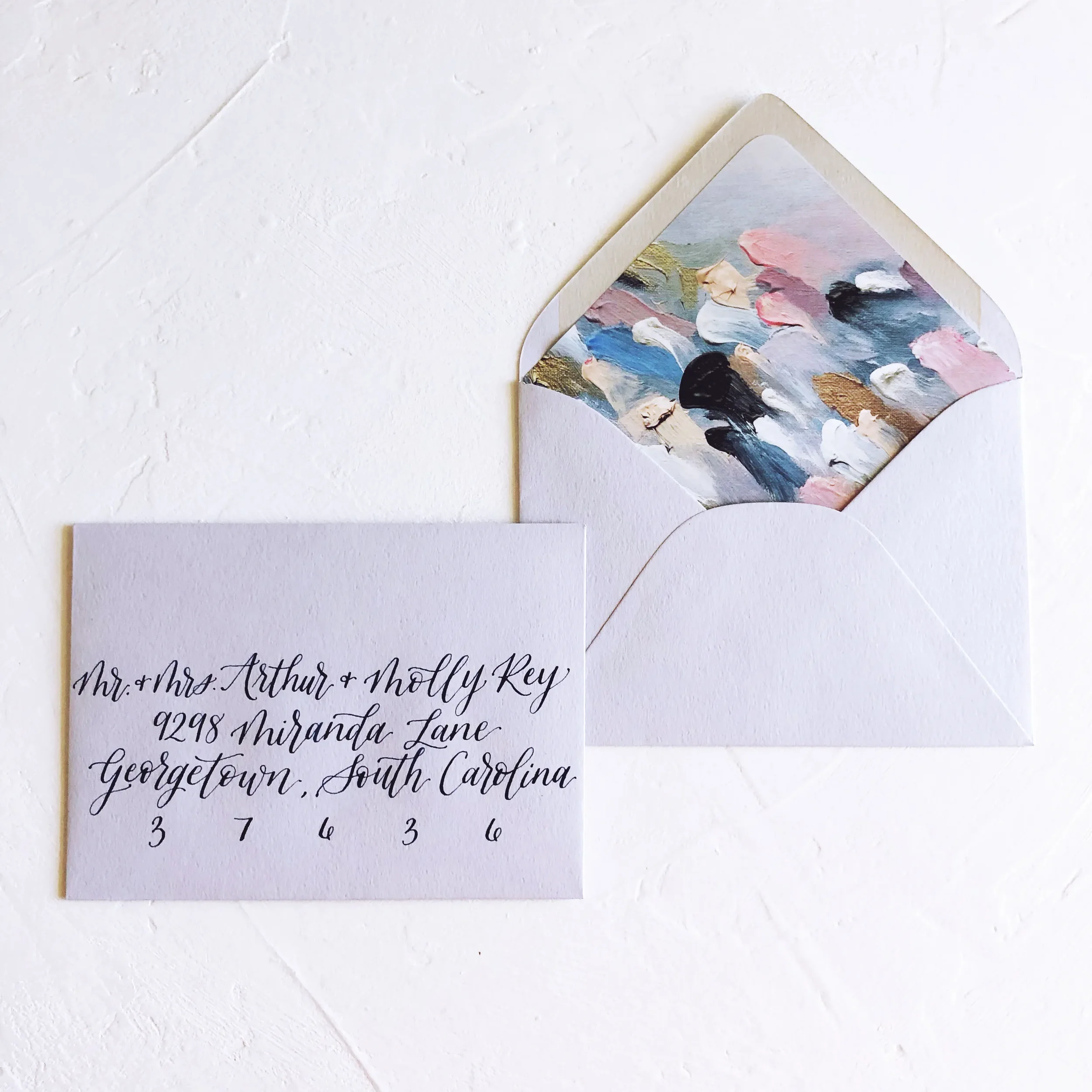 Light dusty blue wedding envelope featuring a custom abstract oil painted liner with gold leaf details and navy blue calligraphy addressing.
