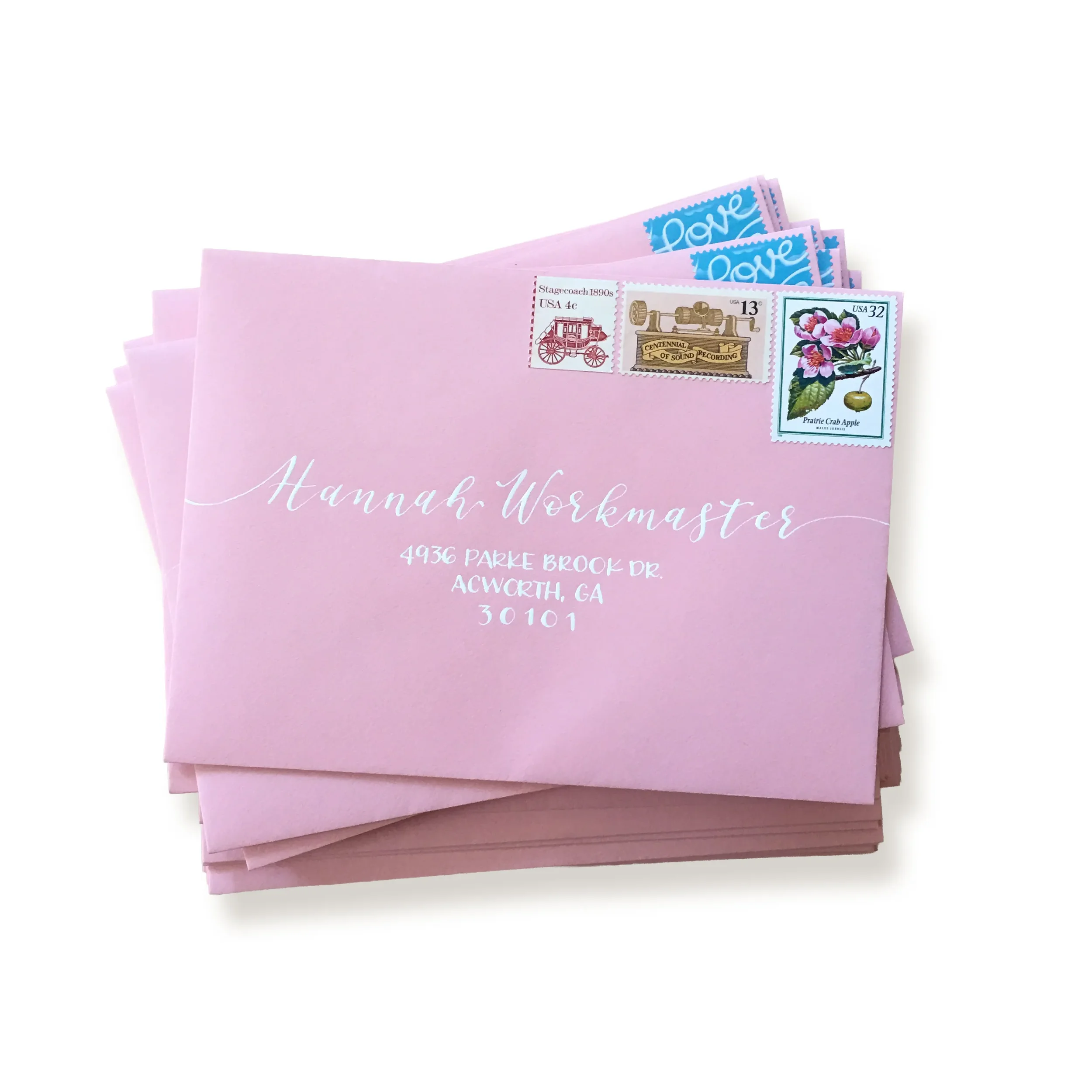 Stack of blush pink bridal shower envelopes with white calligraphy ink addressing and matching vintage postage stamps.