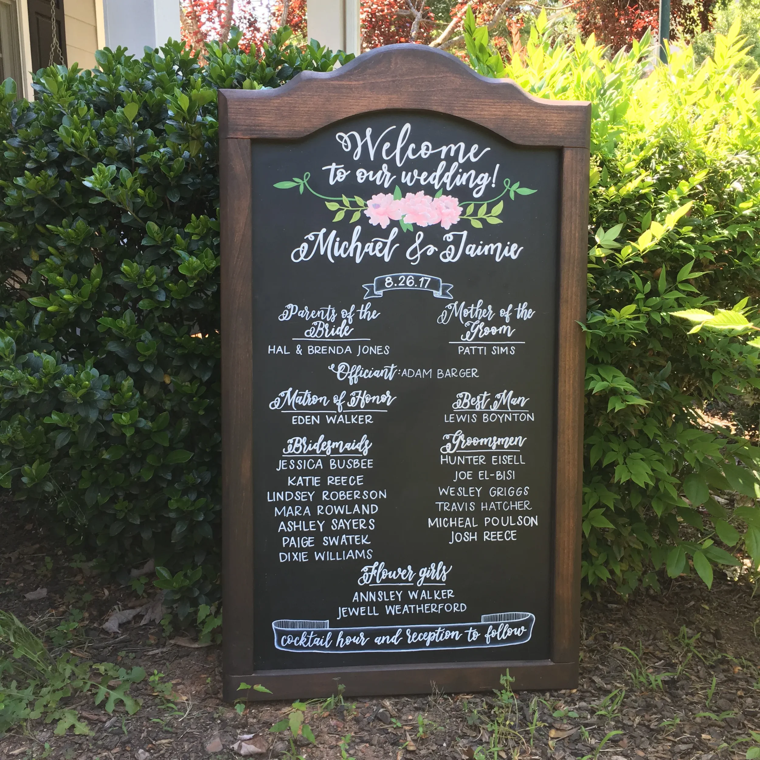 Introduce your loved ones to your guests with a beautifully comprehensive chalkboard wedding party board. Featuring romantic white script typography, crisp block text, and a custom hand-painted pink floral wreath illustration, this welcome board acts