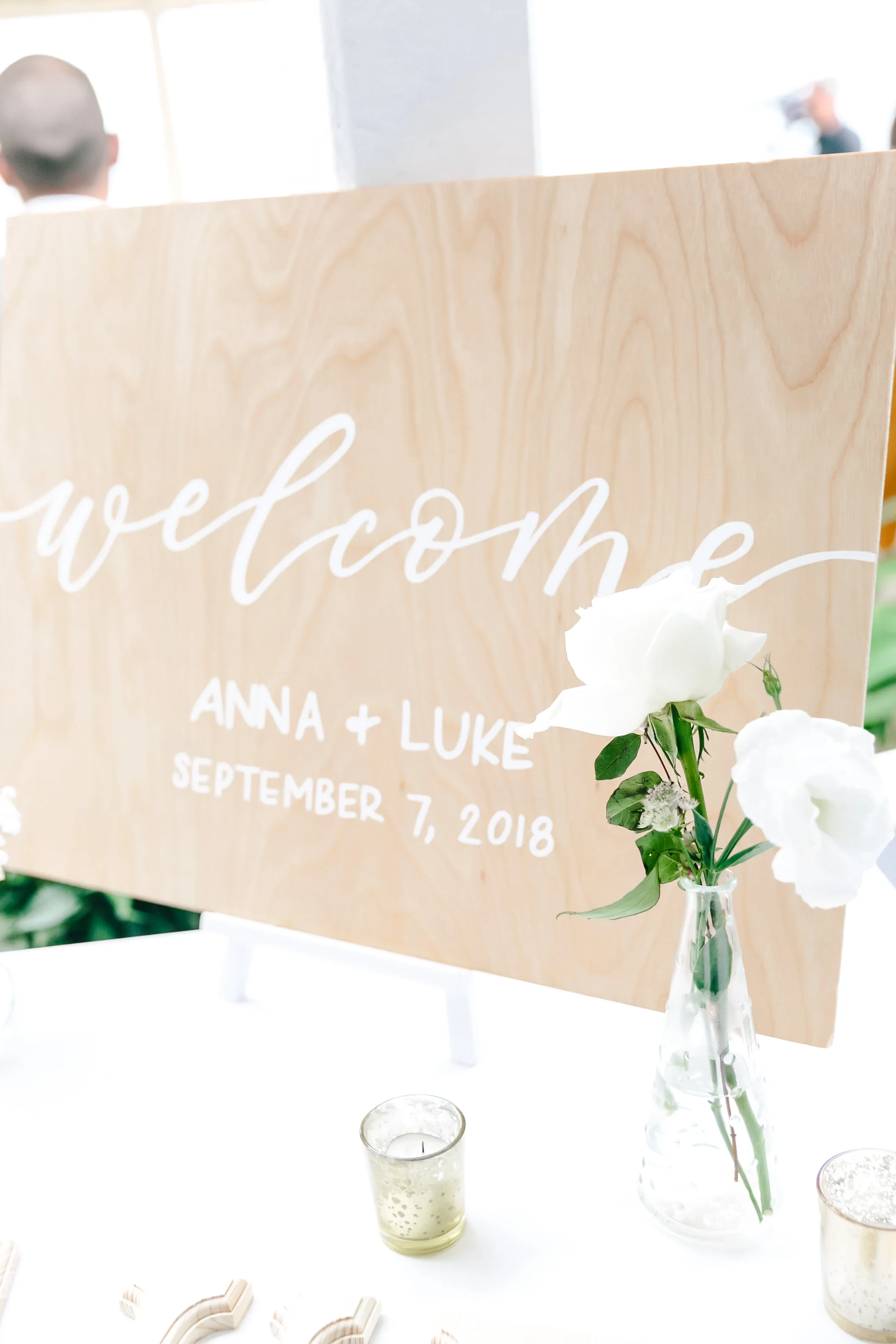 Greet your guests with warm, personalized style using a custom hand-lettered wooden welcome sign. Handcrafted on natural wood with flowing white cursive and clean block lettering, this durable board features the couple's names and wedding date—making